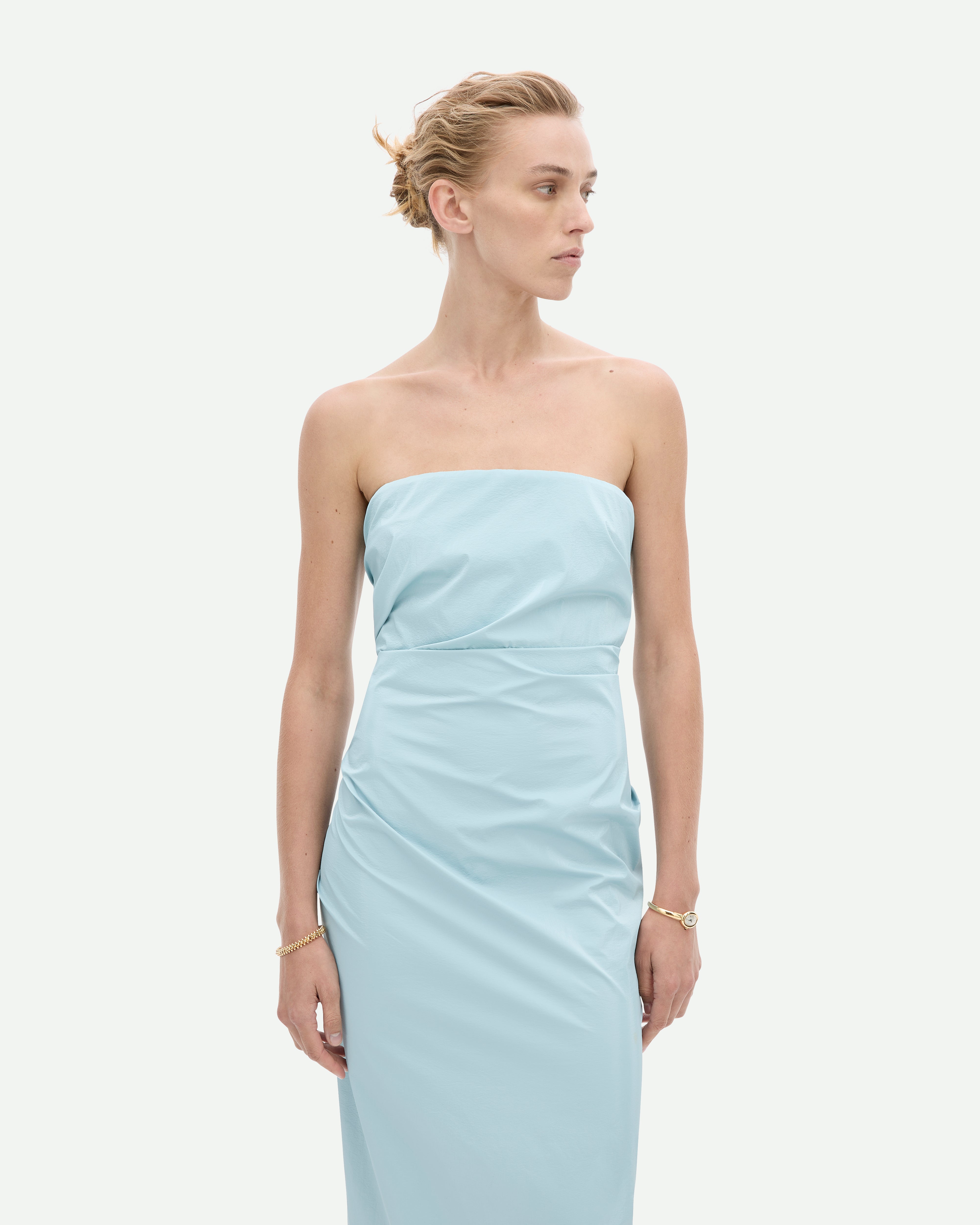 A woman wearing a strapless, sky blue, mid-length dress with a fitted silhouette, Tabloid dress by Common Hours.