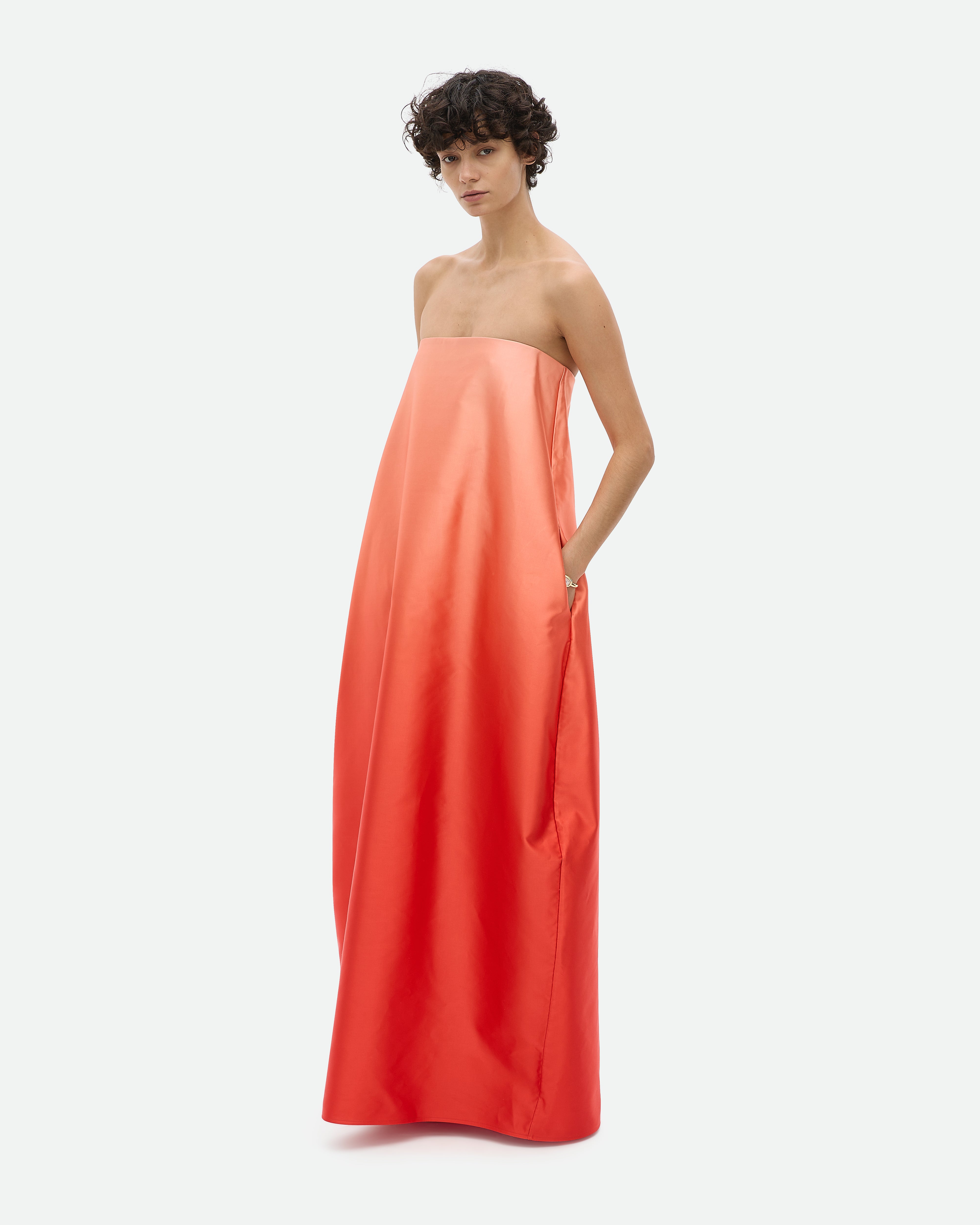 Woman wearing a strapless coral maxi dress Entourage by Common Hours against a white background.