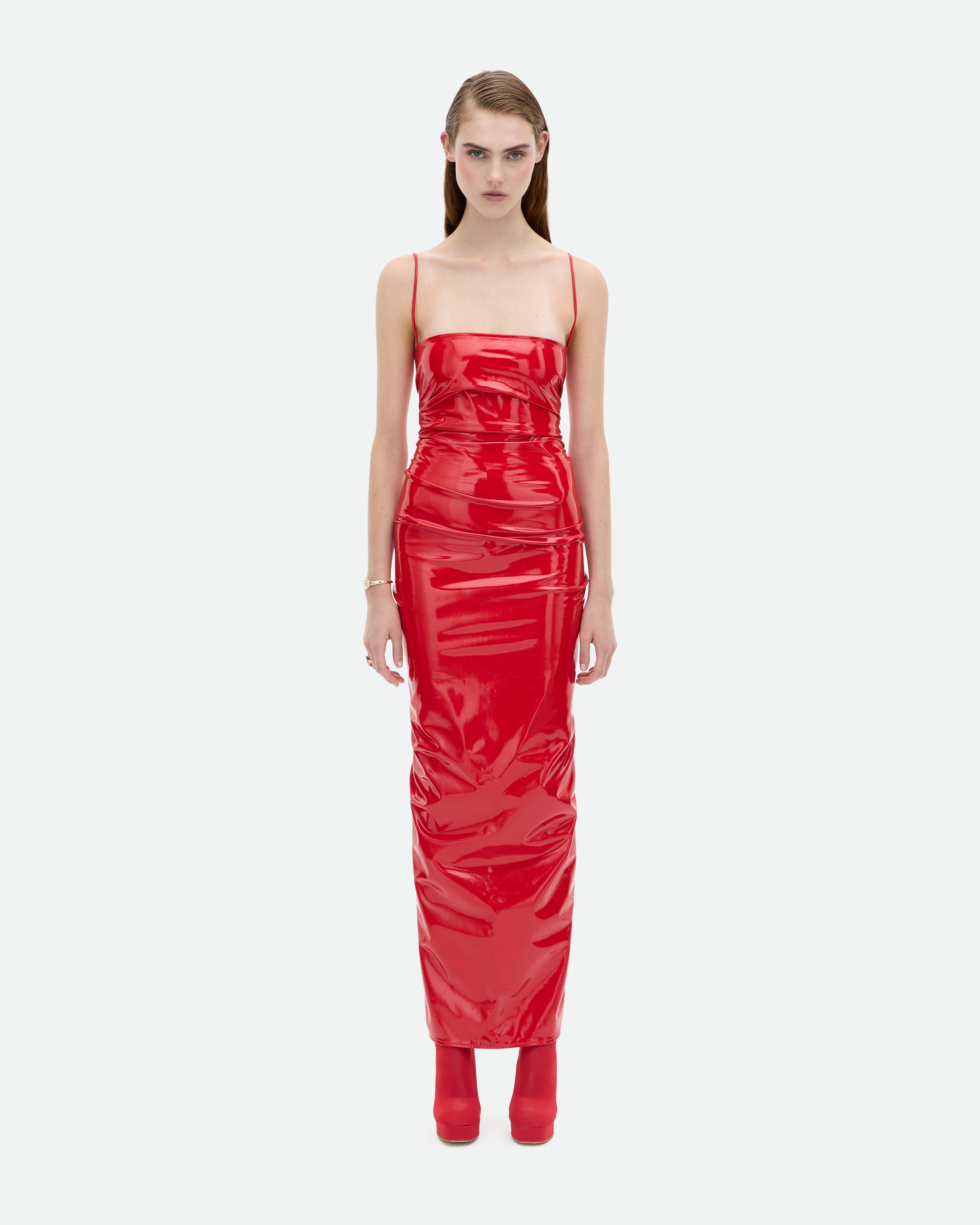 A model wearing a red long stretch Common Hours PVC slip dress with thin straps and matching red boots.