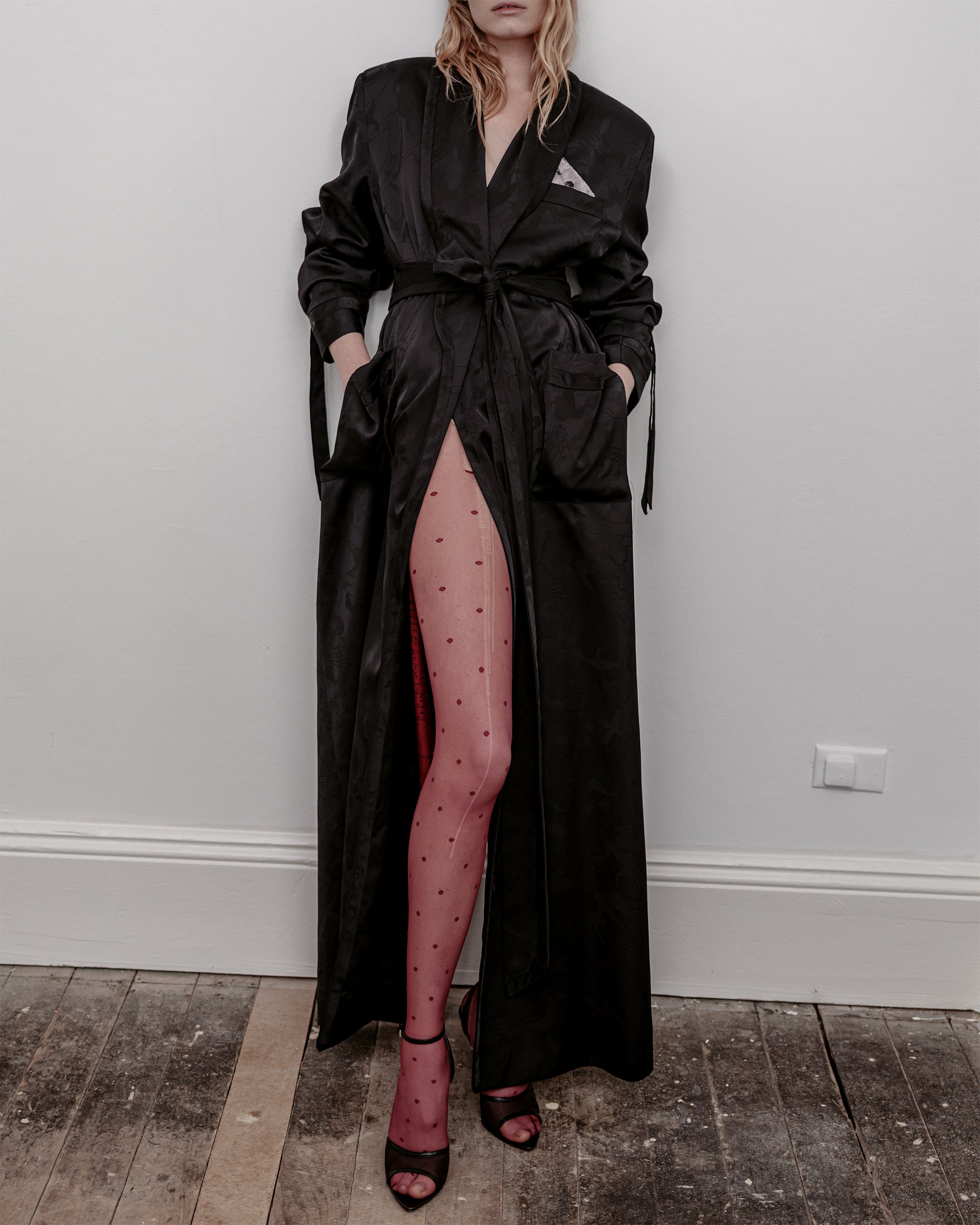 Woman wearing a long black coat Humbug Common Hours dress with red patterned tights.