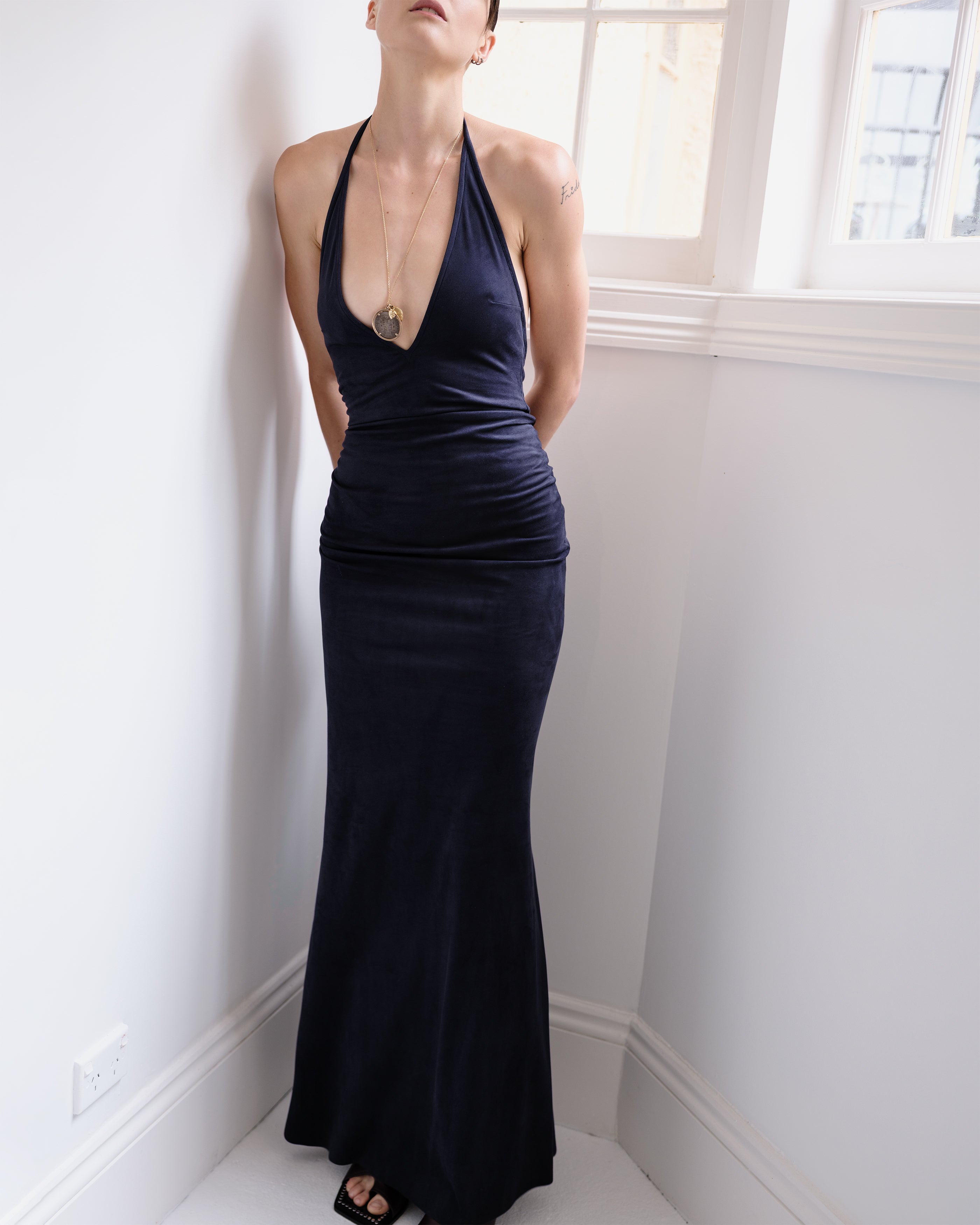 Woman wearing a dark blue suede V-neck evening gown standing against a white wall.
