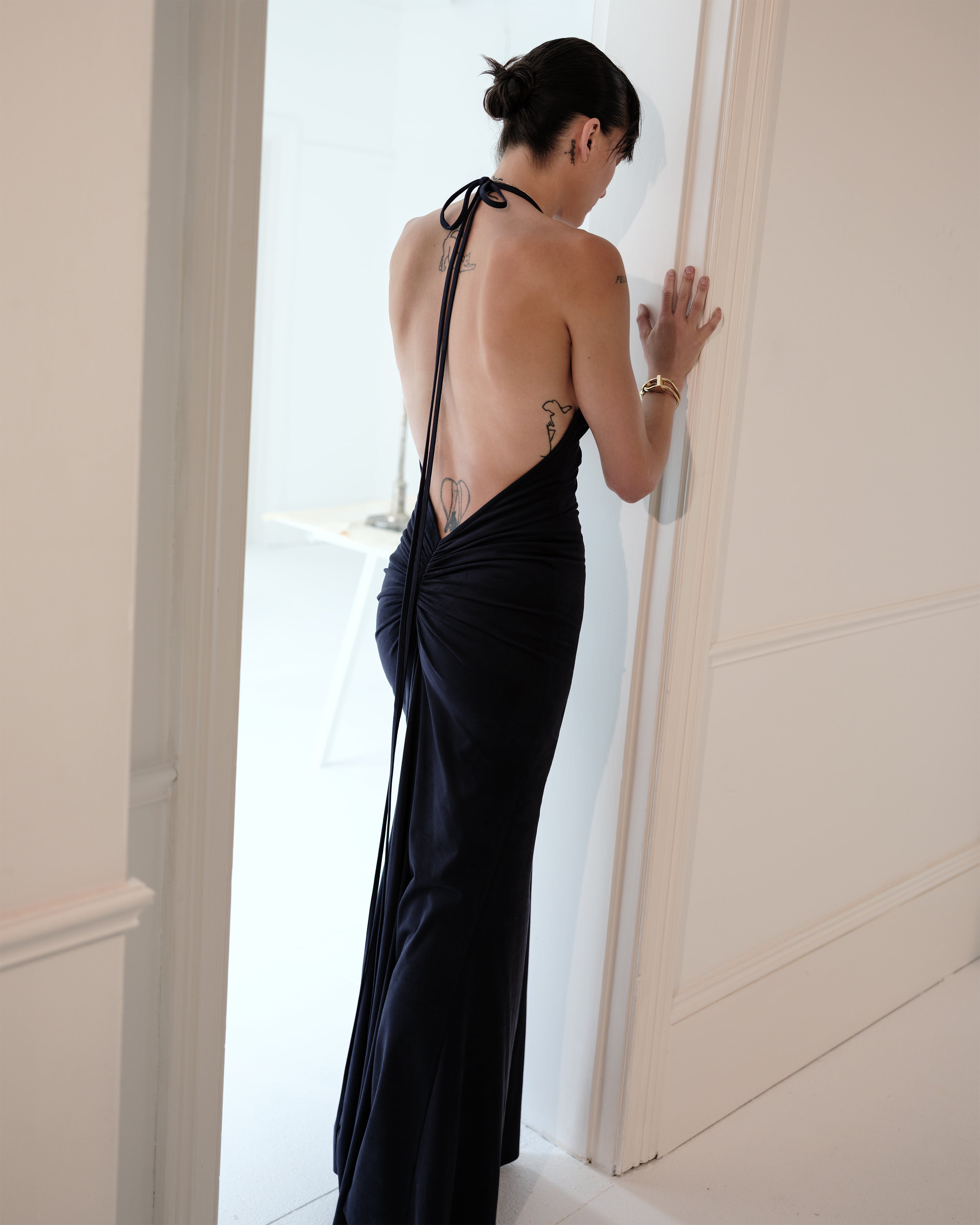 Woman in a navy suede Common Hours evening gown with open back standing in a doorway.