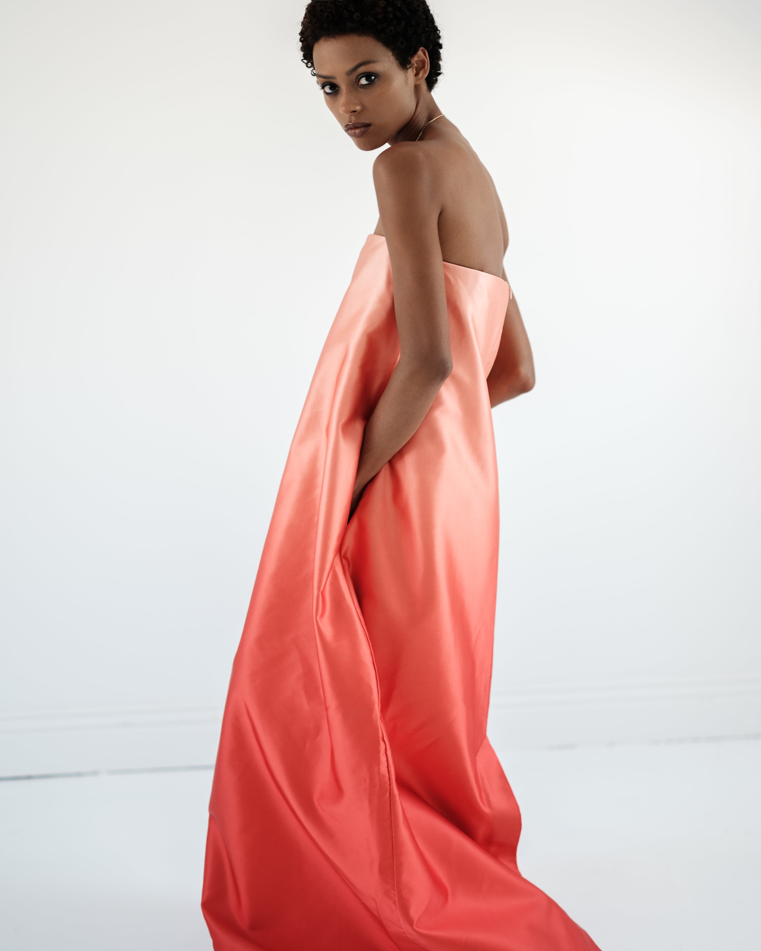 Woman wearing a strapless coral maxi dress Entourage by Common Hours against a white background.