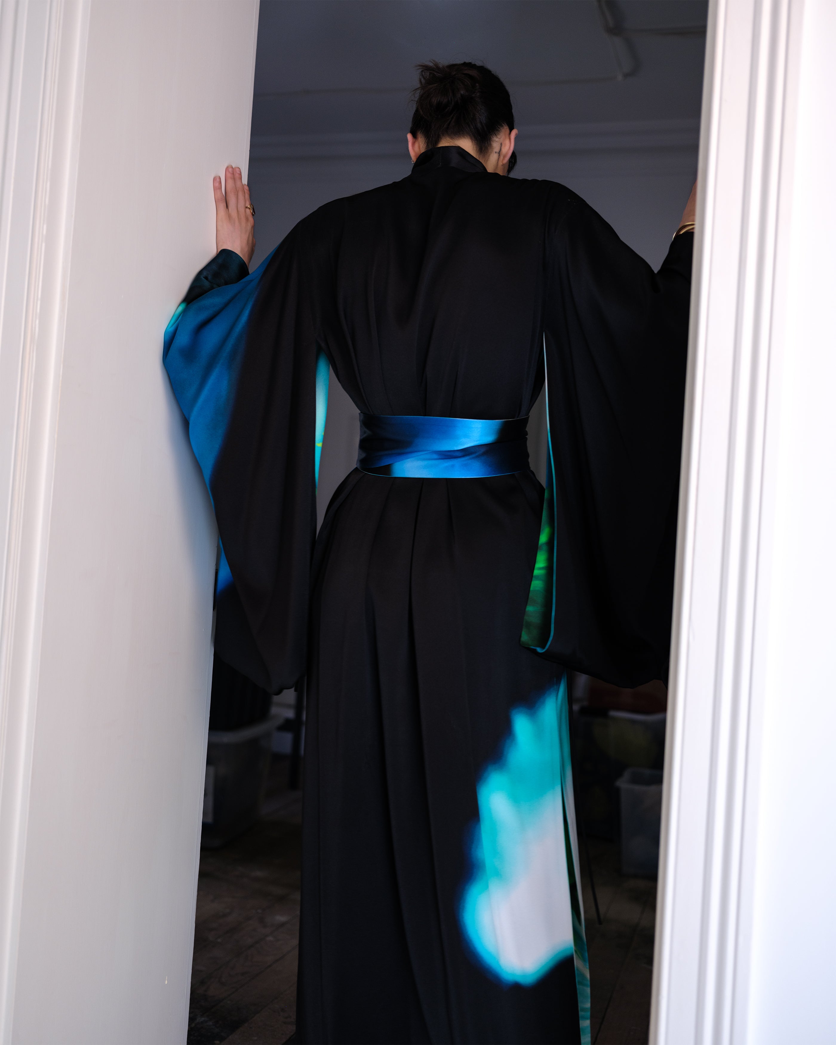 Woman wearing a black and blue reversible silk Common Hours gown standing in a doorway