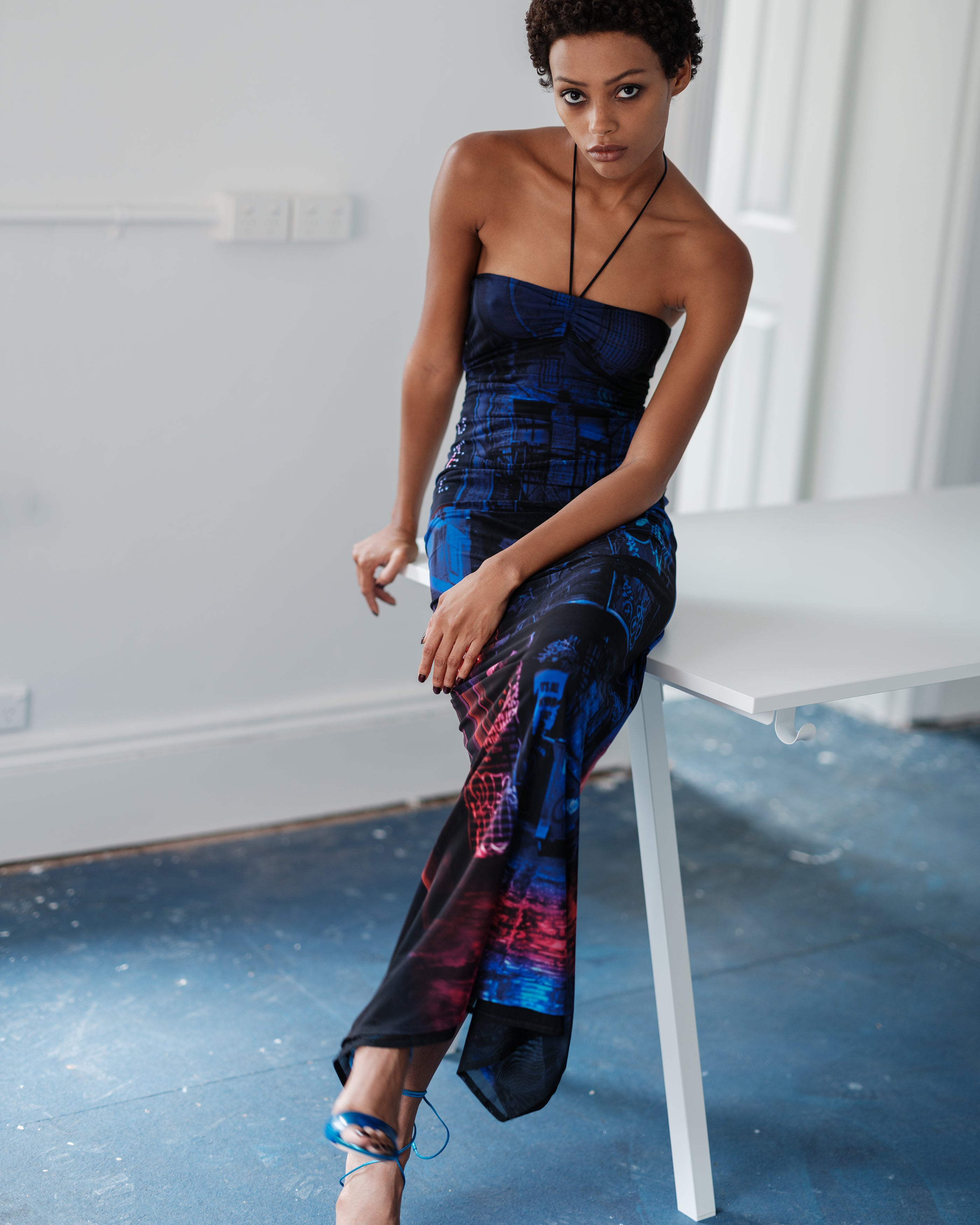 Woman in a halter neck Common Hours dress with a graffiti pattern sitting on a white chair.