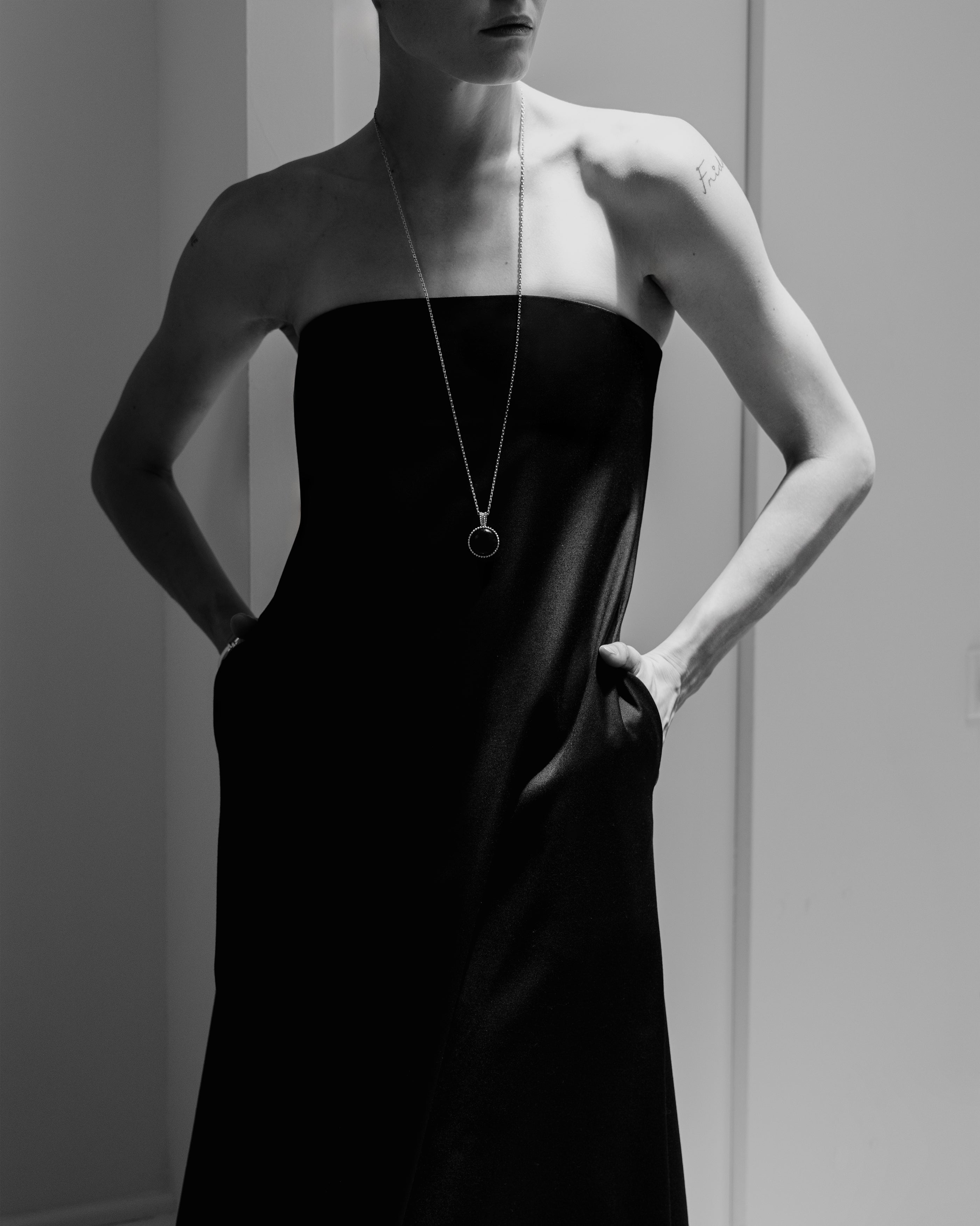 Woman wearing a Common Hours classic black strapless tailored dress in a house.