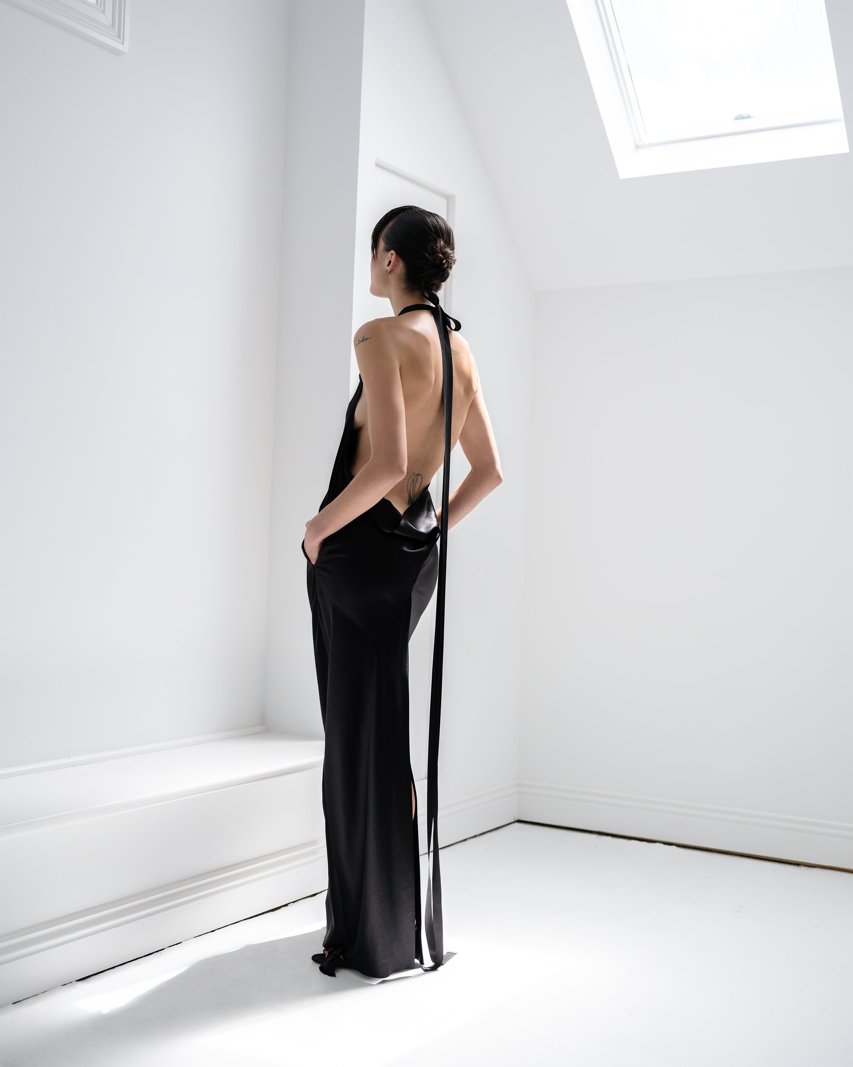 Woman in a black Common Hours evening gown standing in a bright, minimalistic room.