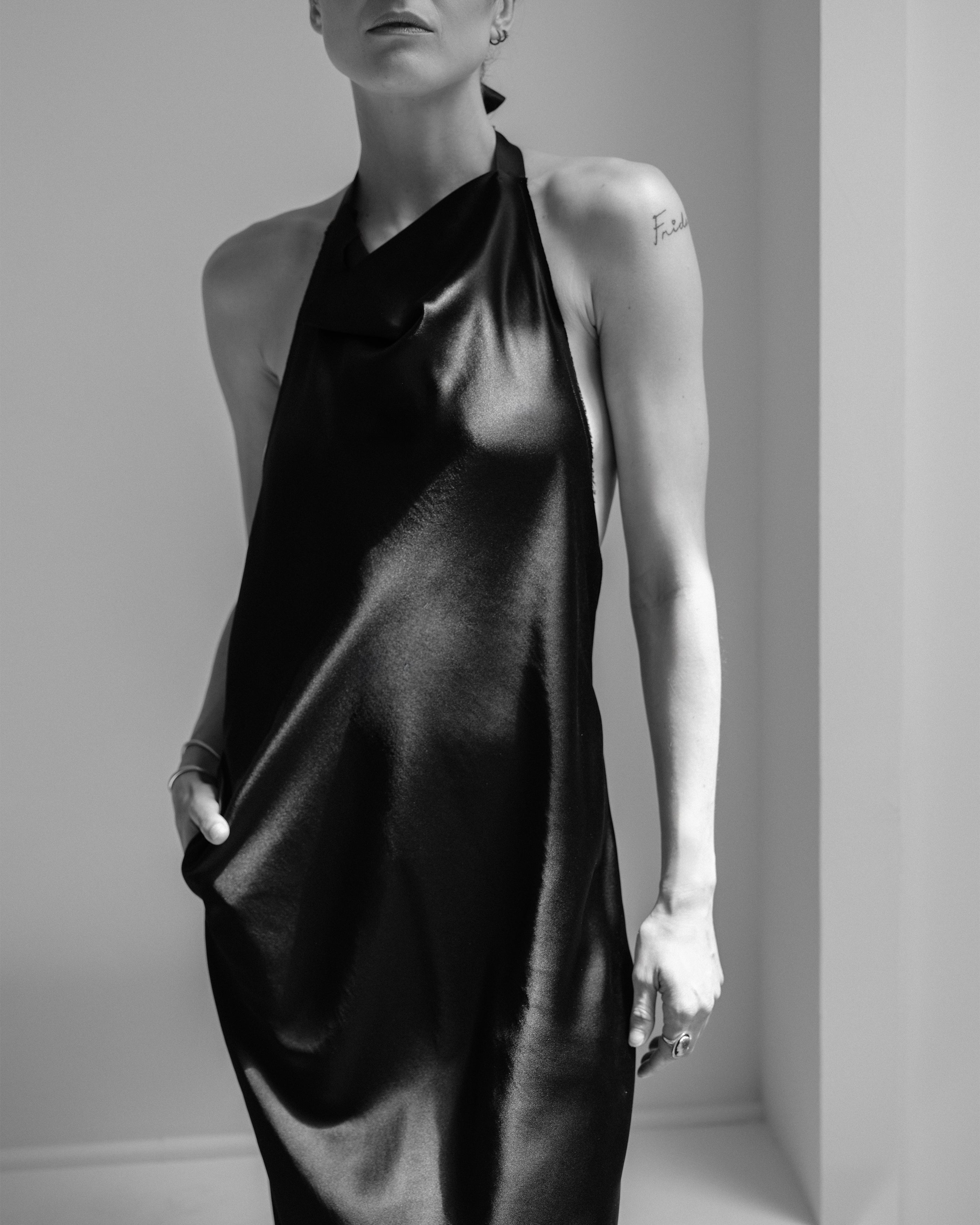 Woman wearing a black Common Hours silk satin halter neck dress against a plain background