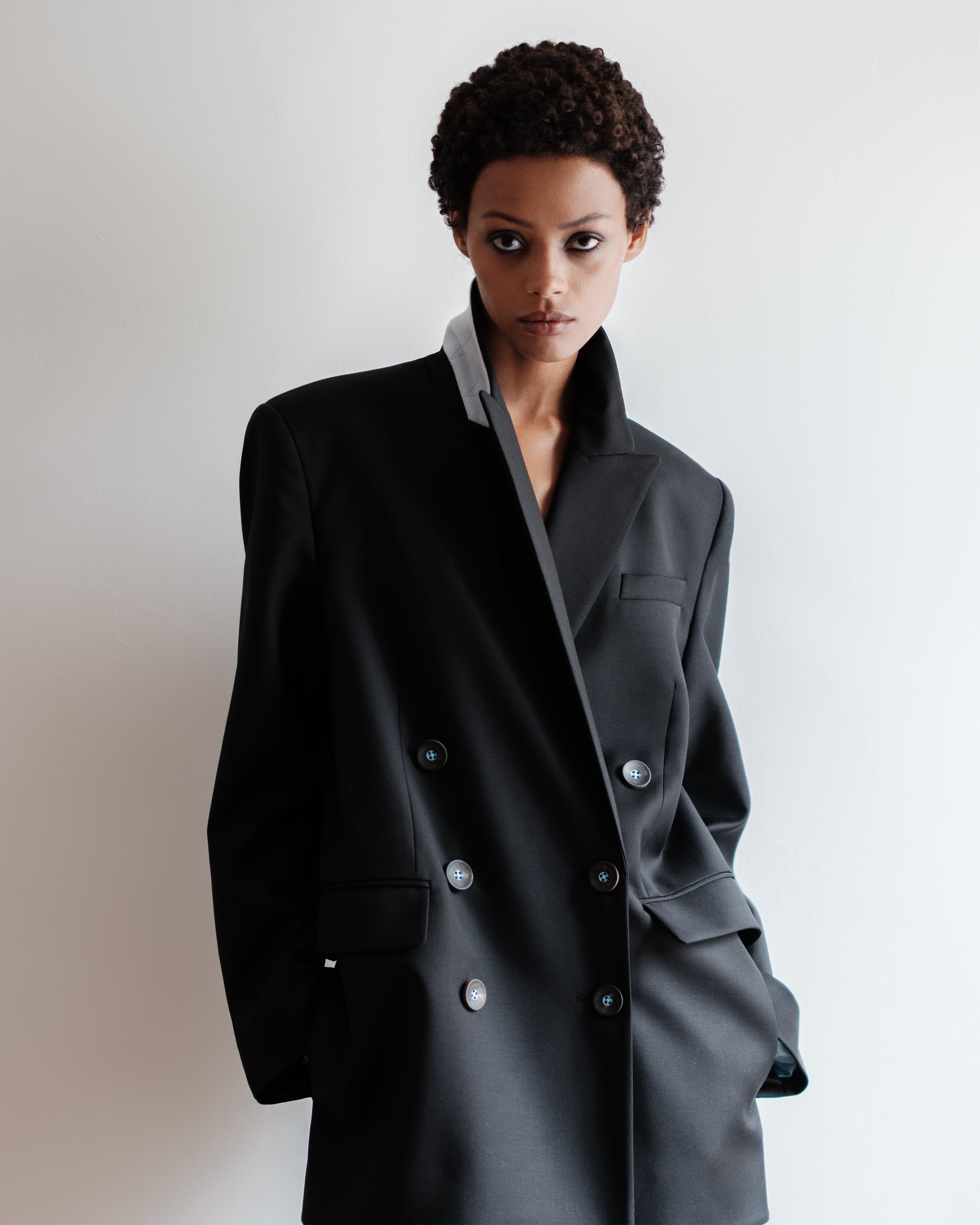 Woman wearing a Common Hours oversized black blazer dress in Italian wool, standing against a white background.