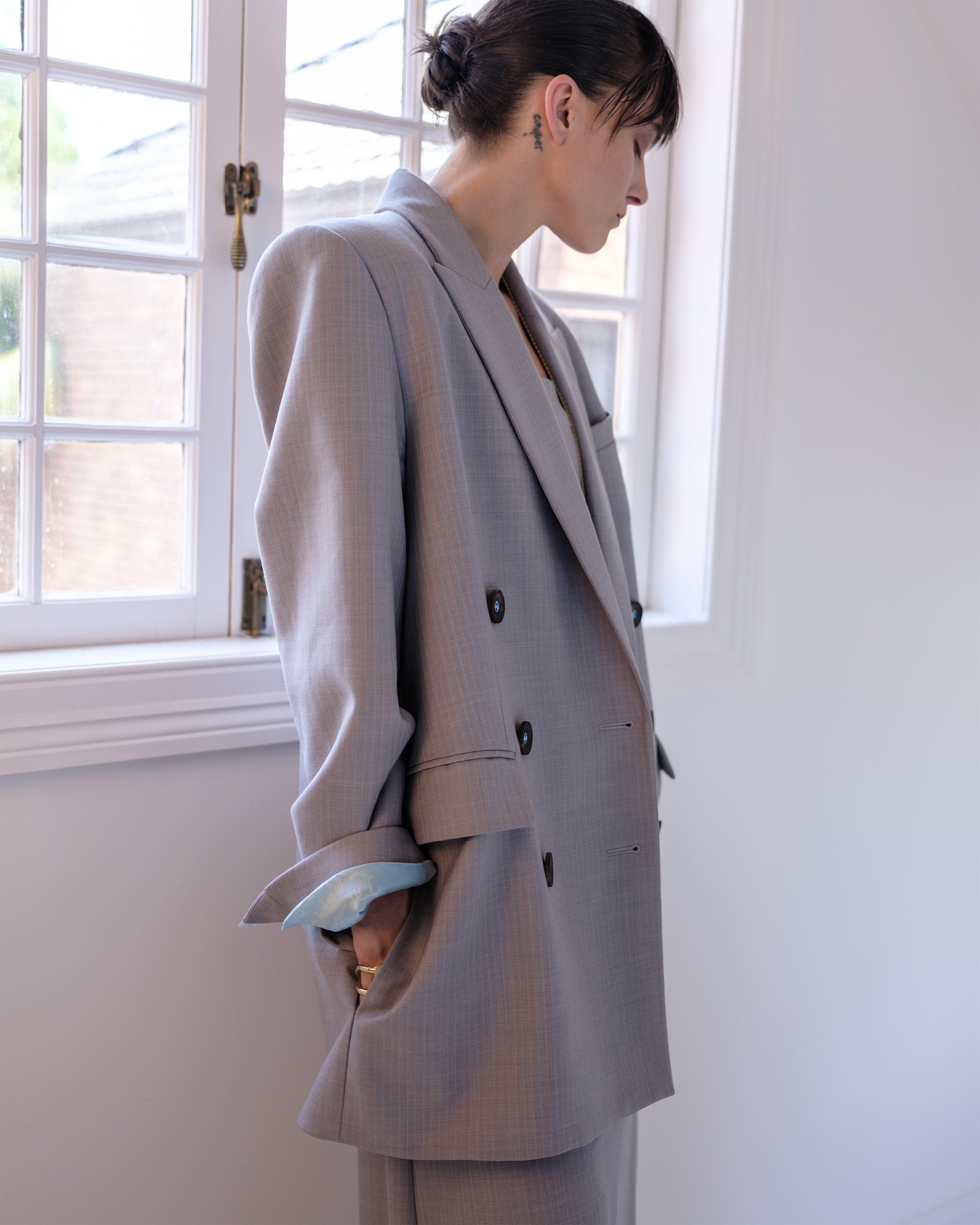 Woman wearing a gray Common Hours tailored blazer and matching dress standing in a room with a window in the background