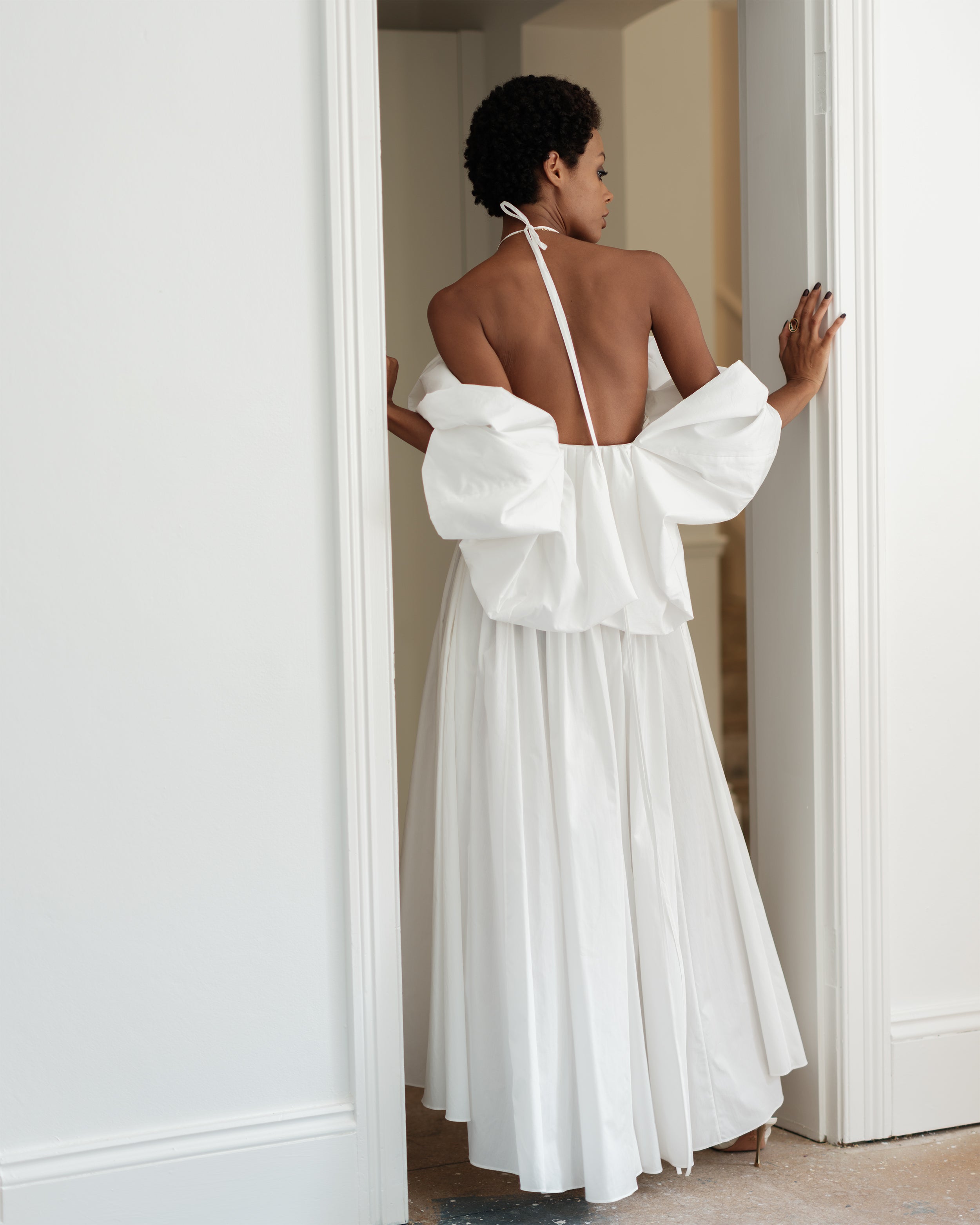 Woman in a white puffy sleeve dress Rounding Errors by Common Hours, standing in a doorway.