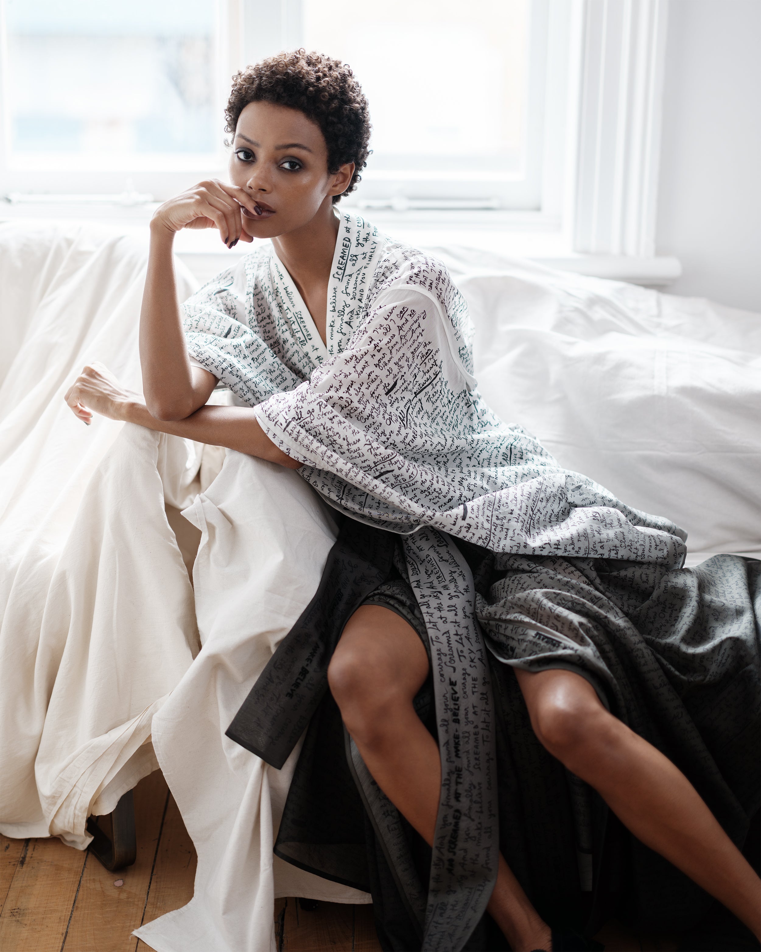 Woman sitting on a couch wearing an ombré Common Hours robe dress with printed and hand-embroidered lyrics