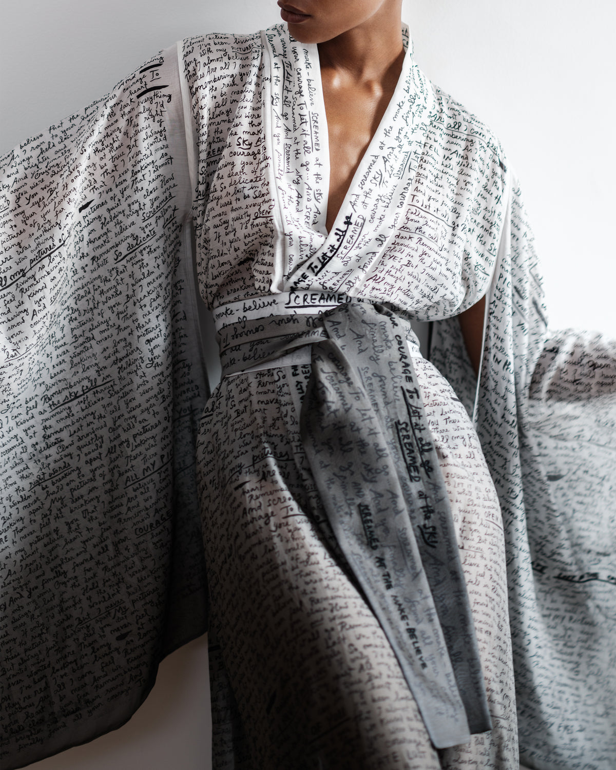 Woman wearing a Common Hours silk cotton robe with printed and hand-embroidered lyrics on a plain background