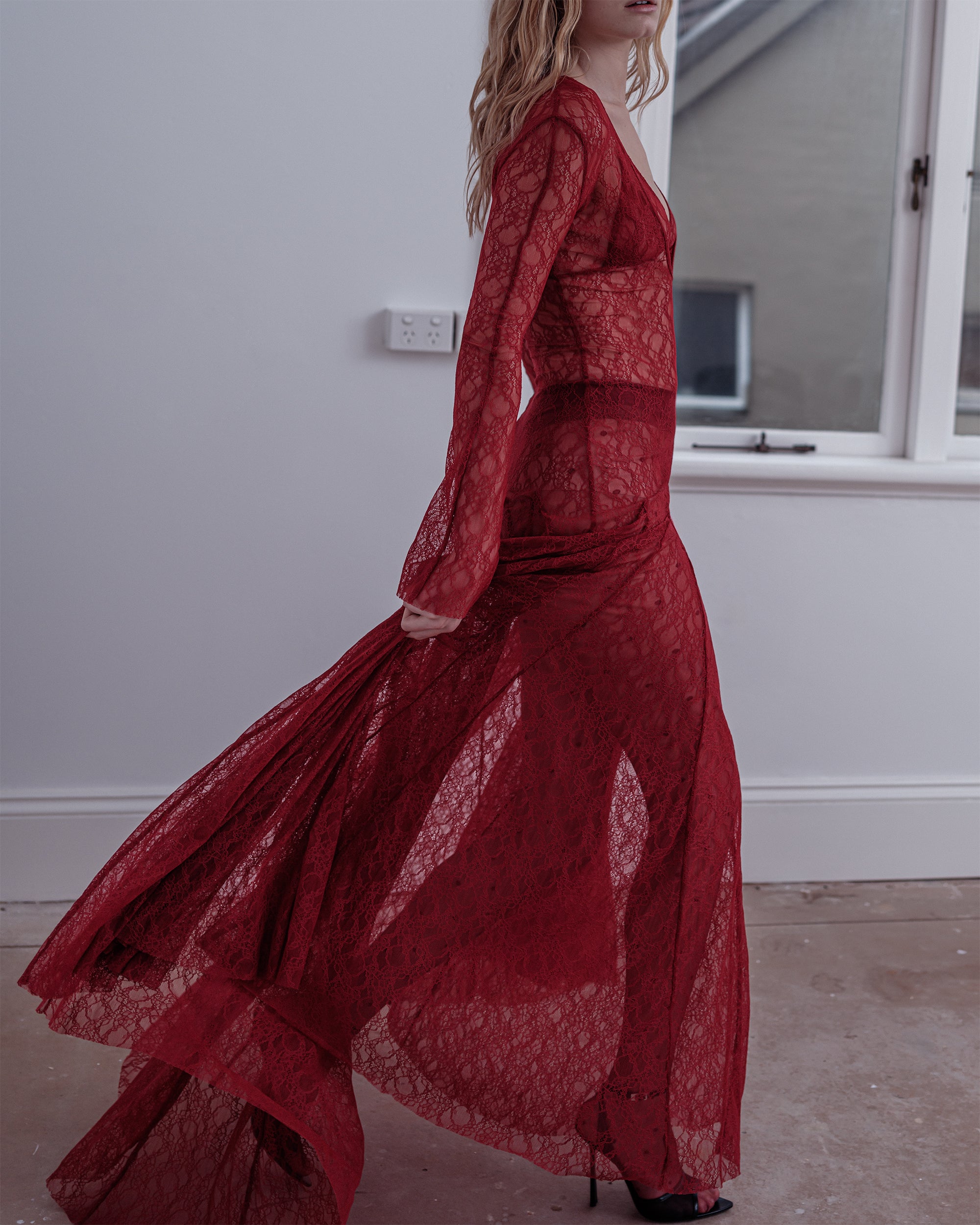 Woman walking with a Common Hours see-through red lace dress with long flare sleeve.