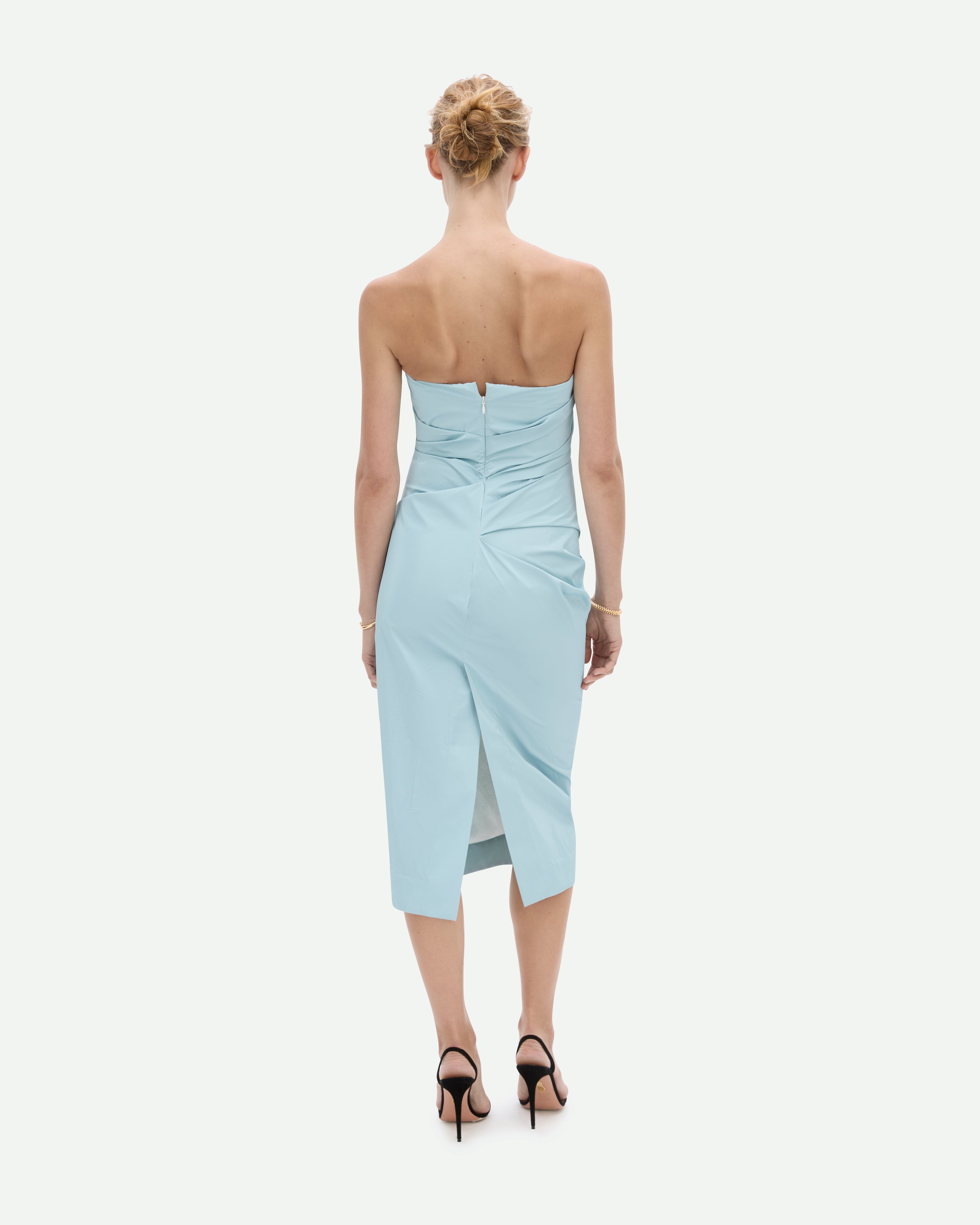 A woman wearing a strapless, sky blue, mid-length dress with a fitted silhouette, Tabloid dress by Common Hours.