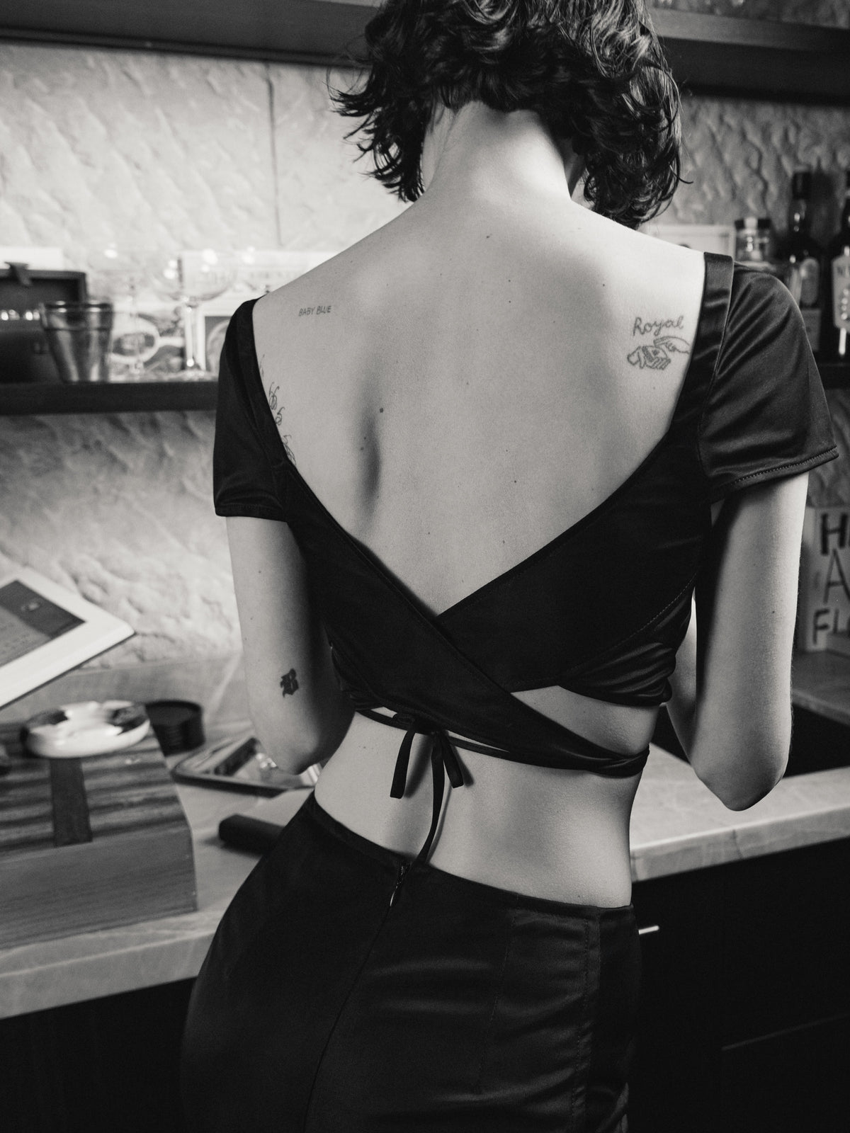 The Common Hours x Abbey Lee Unfolding Top is a lingerie-inspired short-sleeve, cross-over wrap crop top in black.