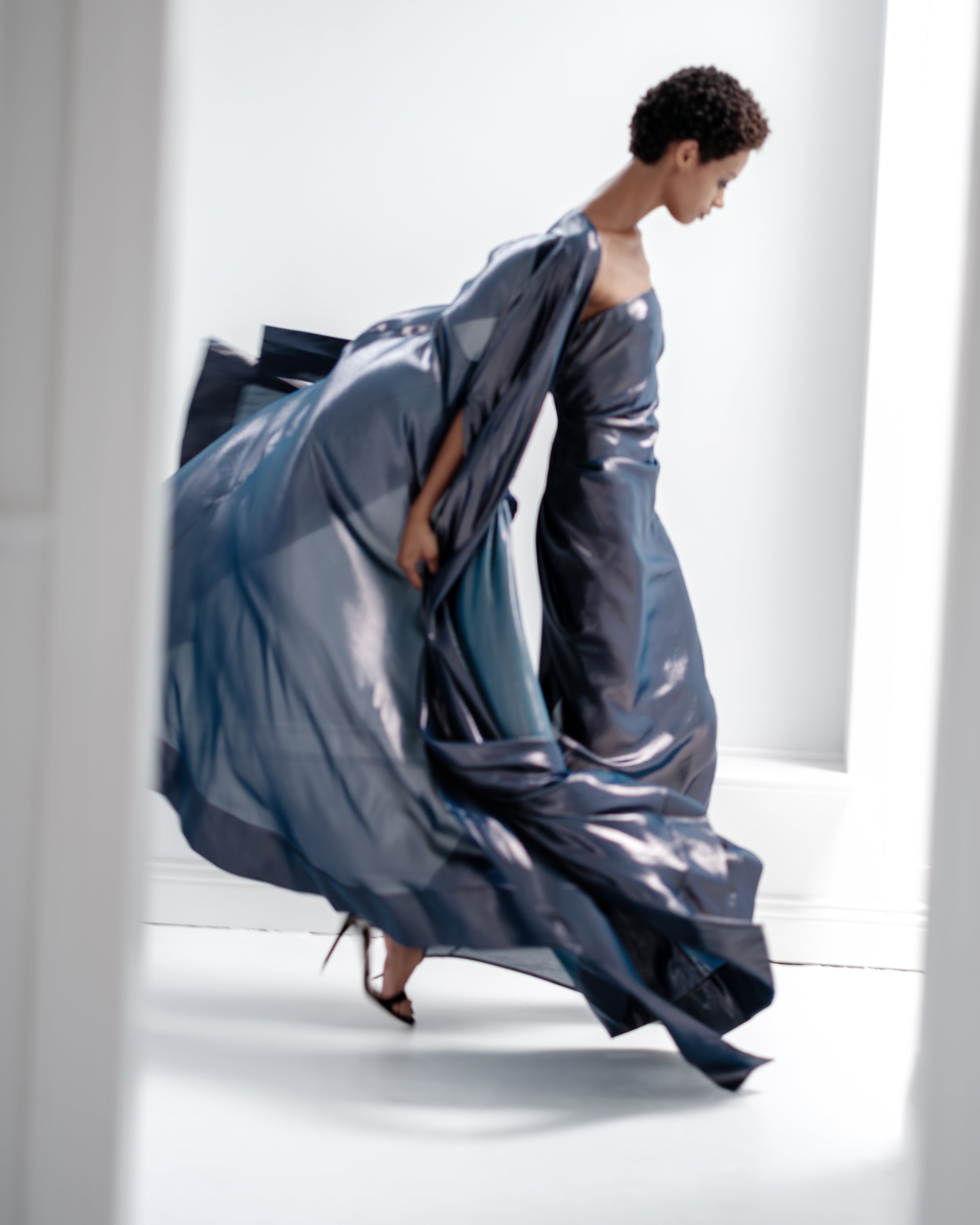 Woman wearing a strapless Common Hours blue gown and matching cape against a white background