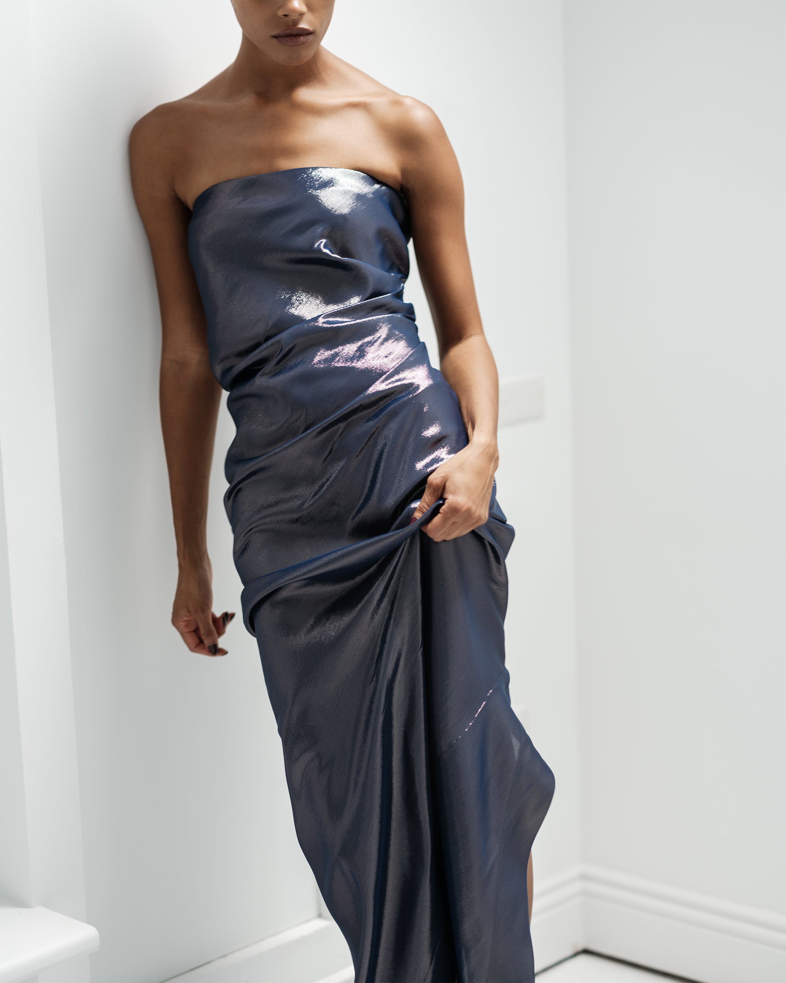 Woman wearing a strapless metallic Common Hours navy blue dress against a white background