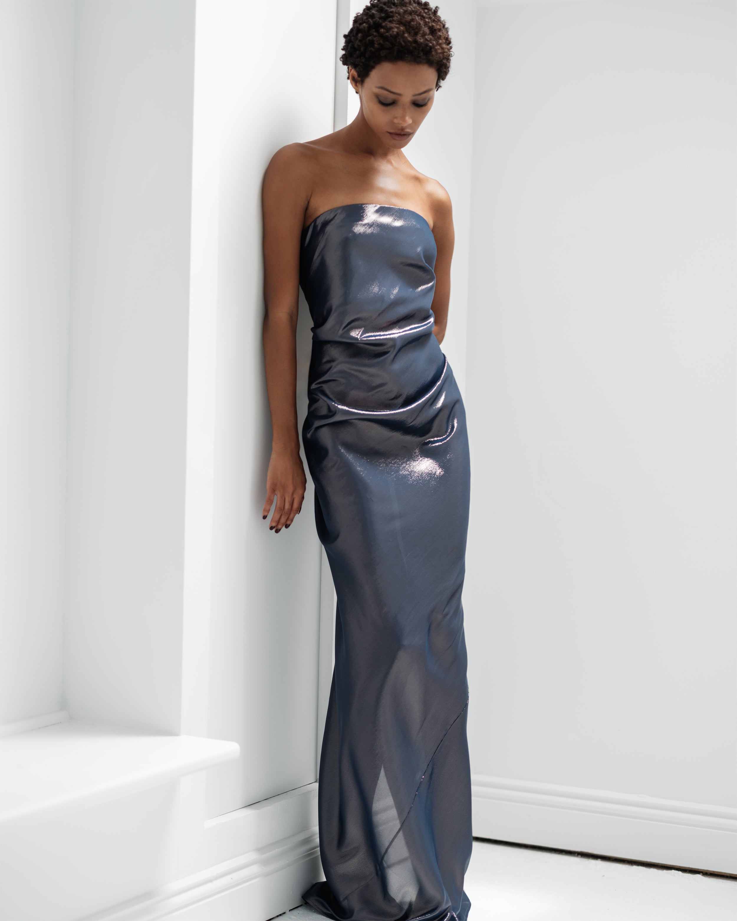 Woman wearing a strapless Common Hours midnight blue evening gown against a white wall