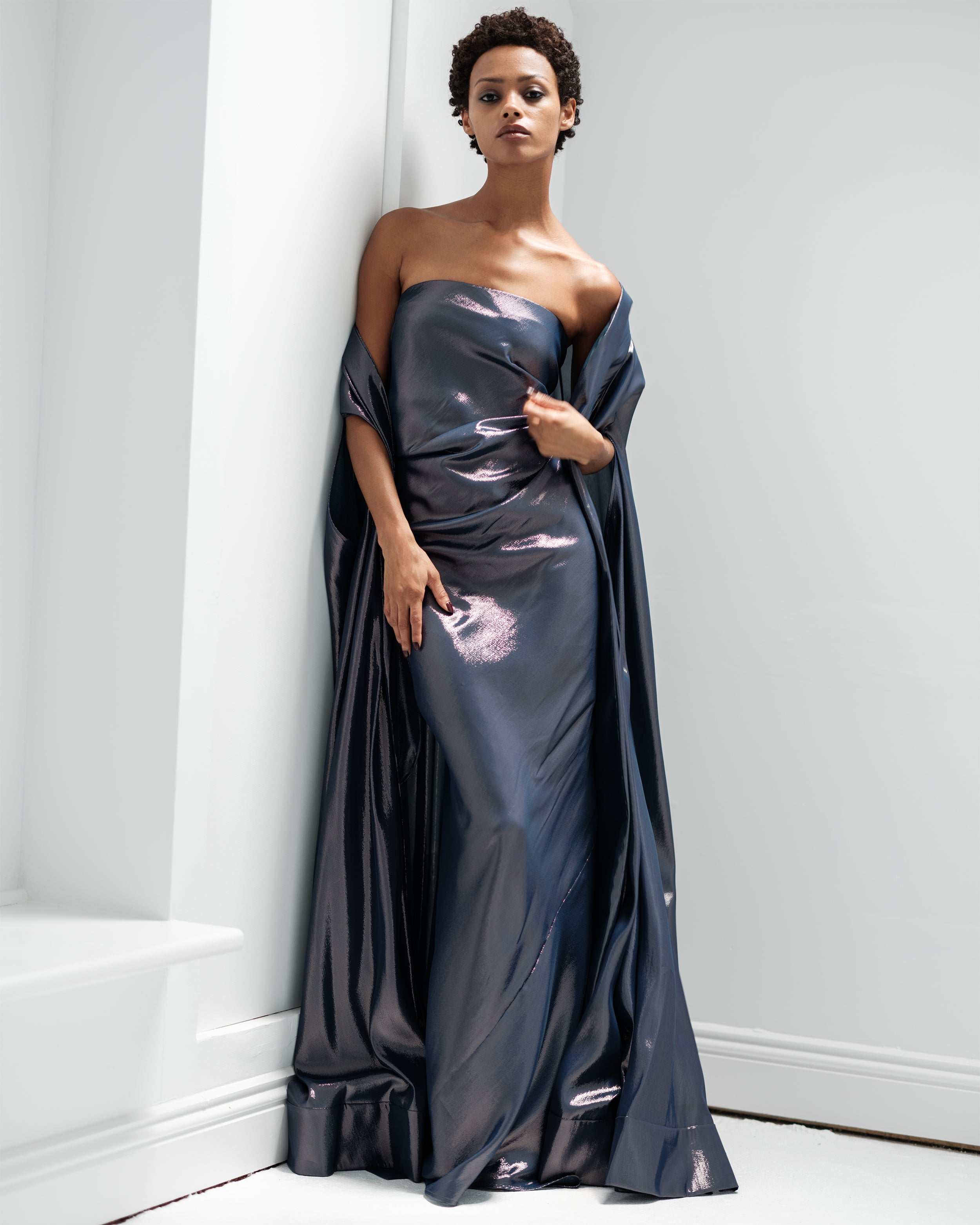 Woman wearing a dark blue strapless Common Hours gown against a white wall