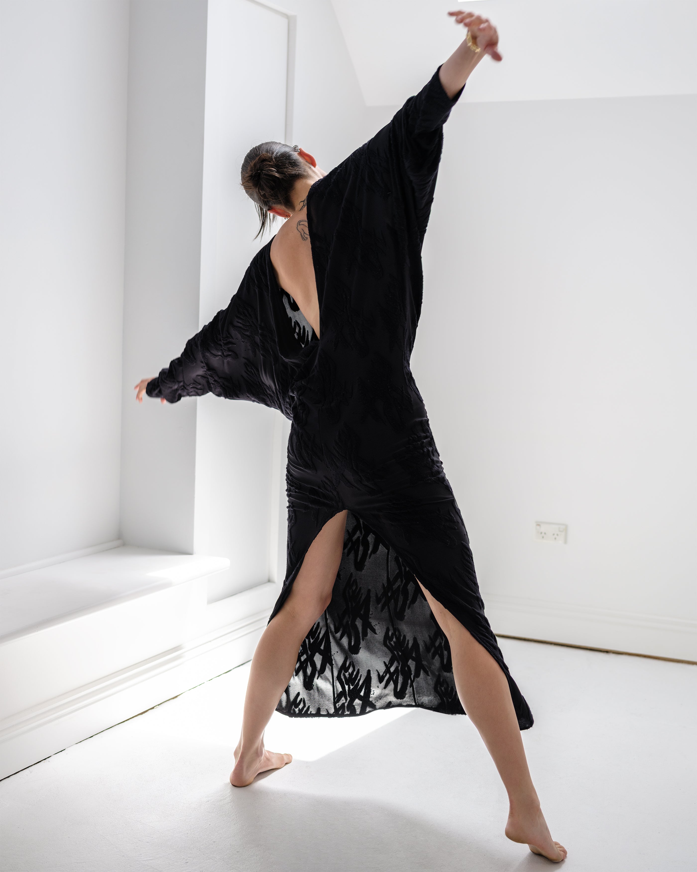 Woman in a Common Hours Offset black dress dancing in a white room.