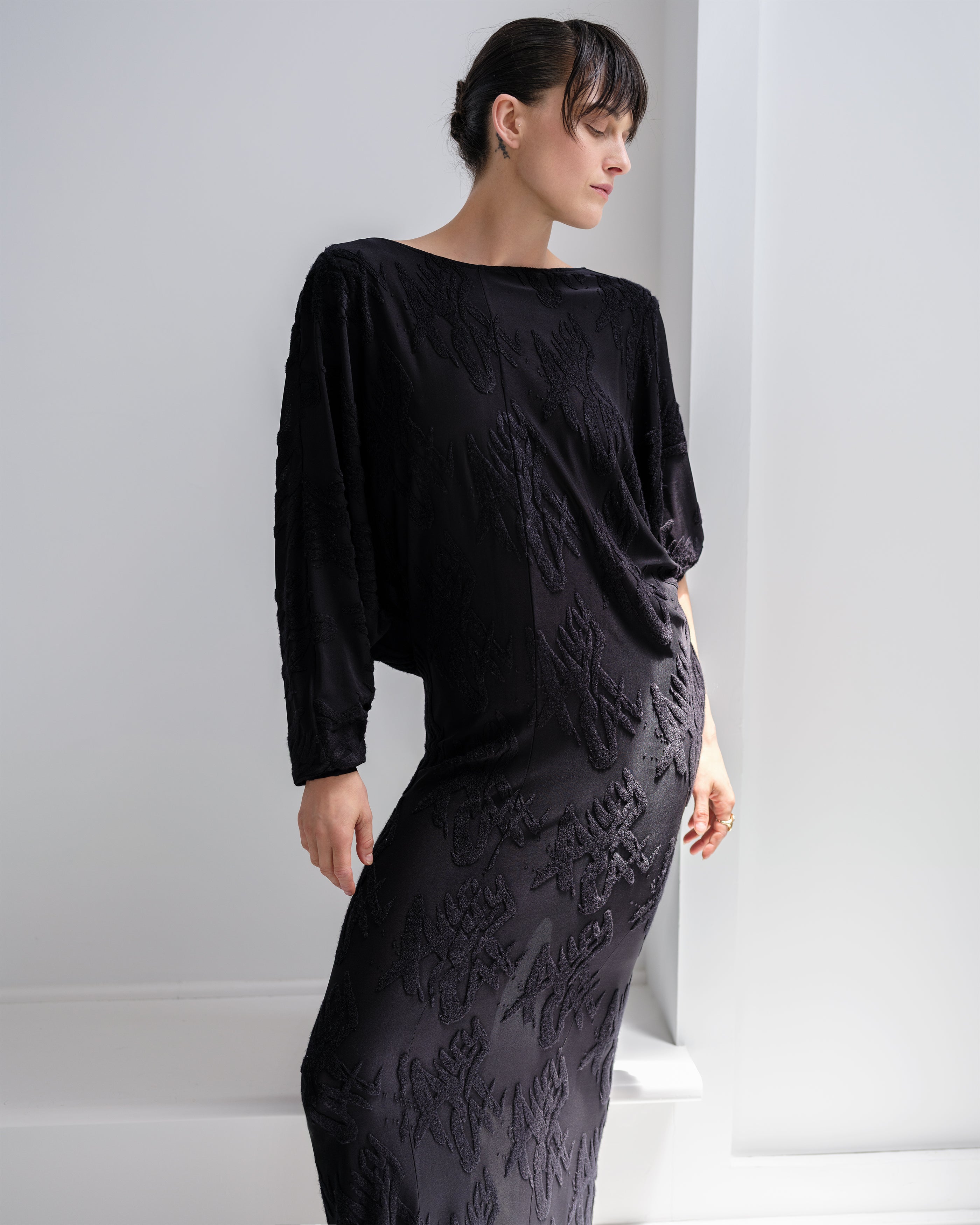 Woman wearing a black Common Hours Offset dress with a jacquard pattern against a white background.