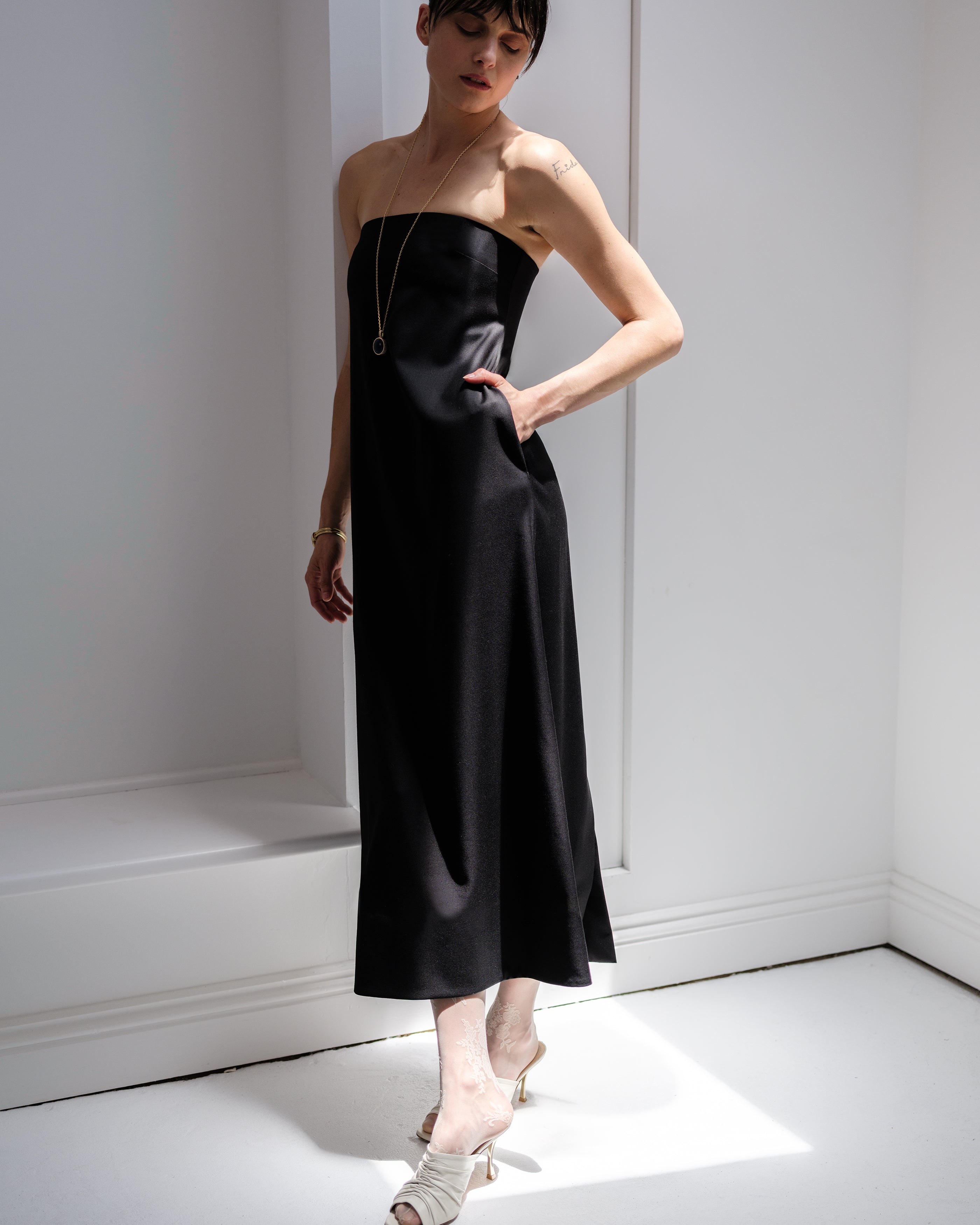 Woman wearing a black Common Hours strapless dress in a minimal white room.