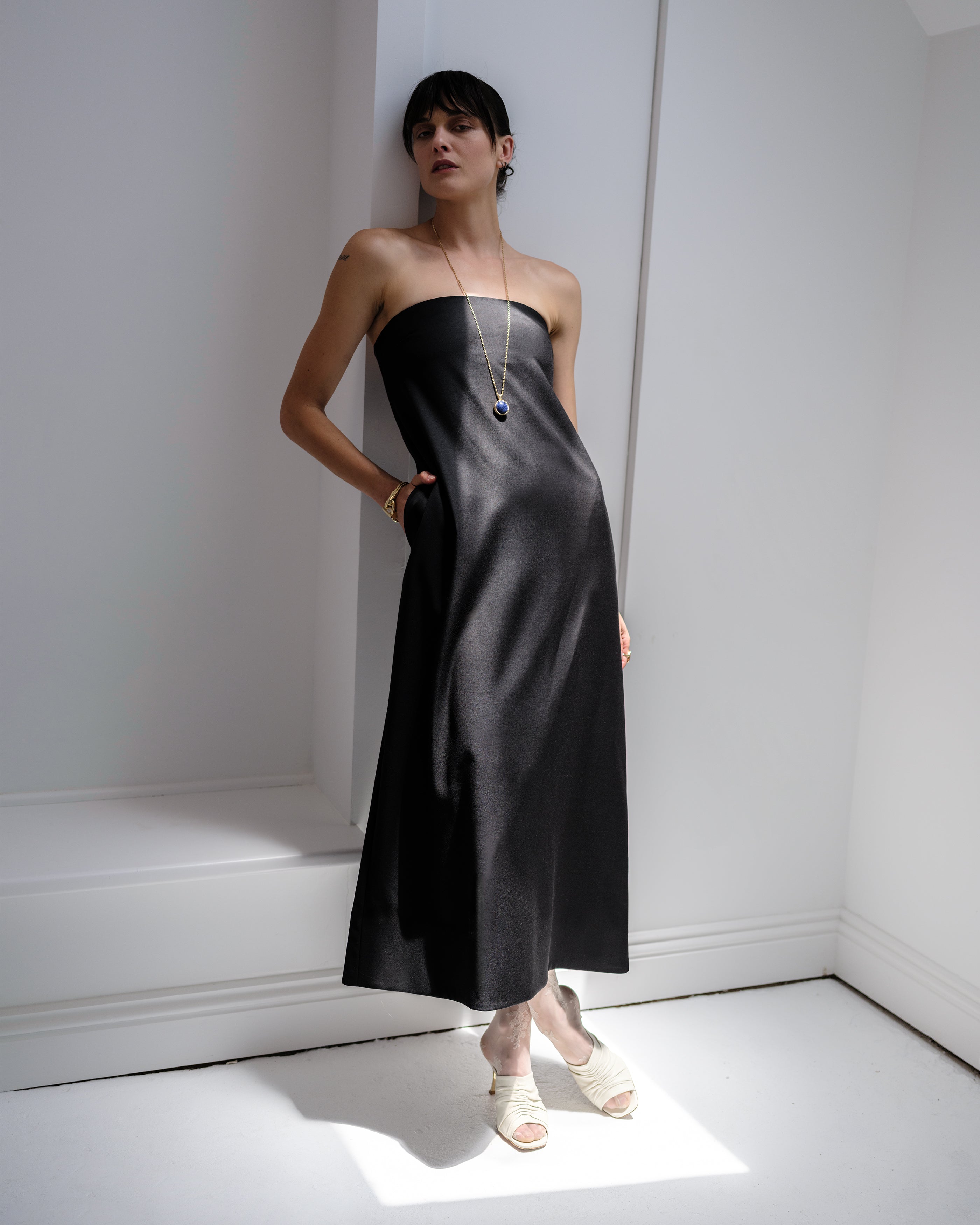 Woman wearing a black strapless Common Hours dress in a minimal white room.