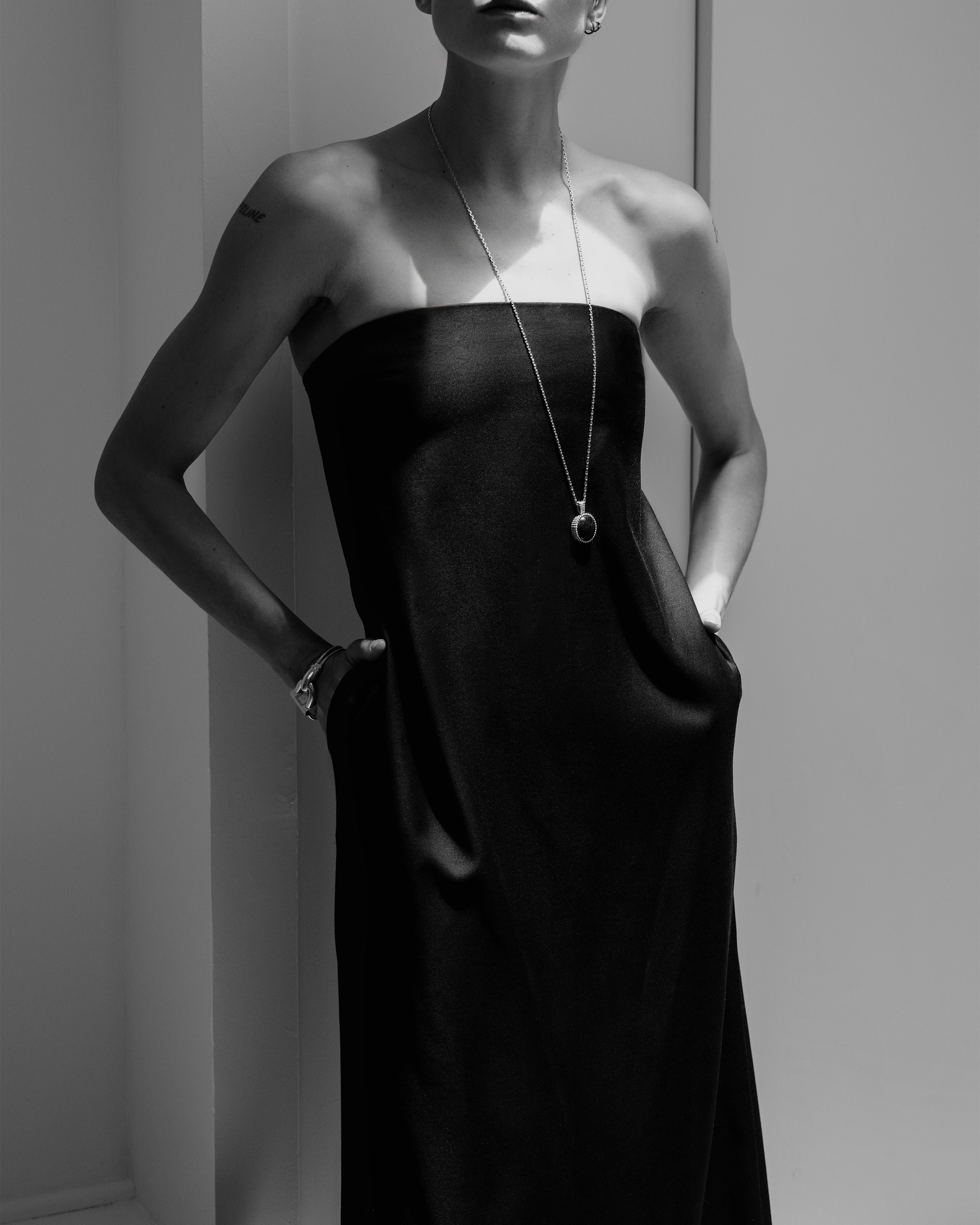 Woman wearing a black Common Hours strapless dress with a necklace against a neutral background.