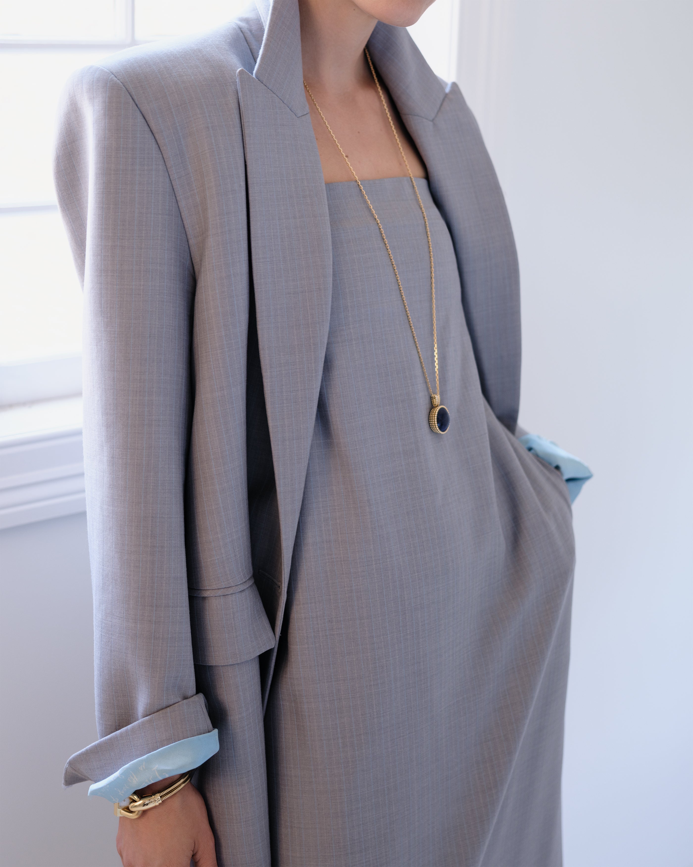 Woman wearing a gray Common Hours suit jacket and strapless dress with a white background.