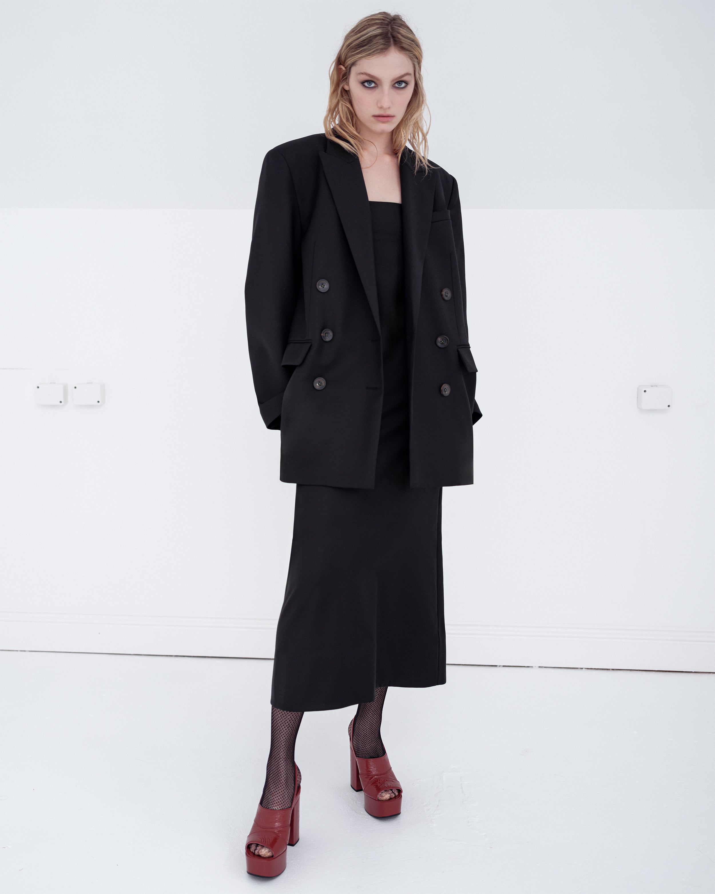 Woman wearing a black Common Hours oversized blazer and matching strapless dress on a white background
