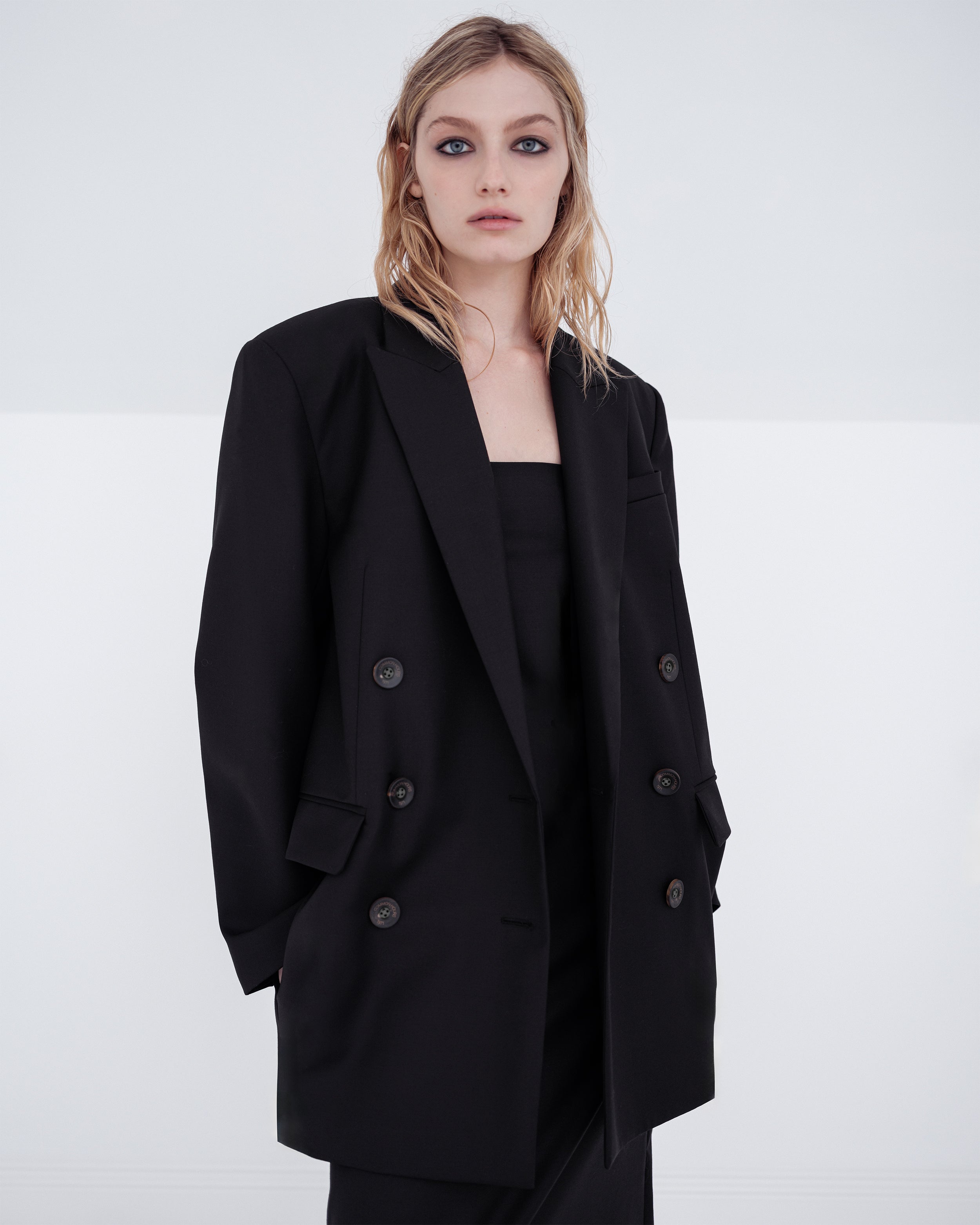 Woman wearing a black Common Hours blazer and matching strapless dress on a white background