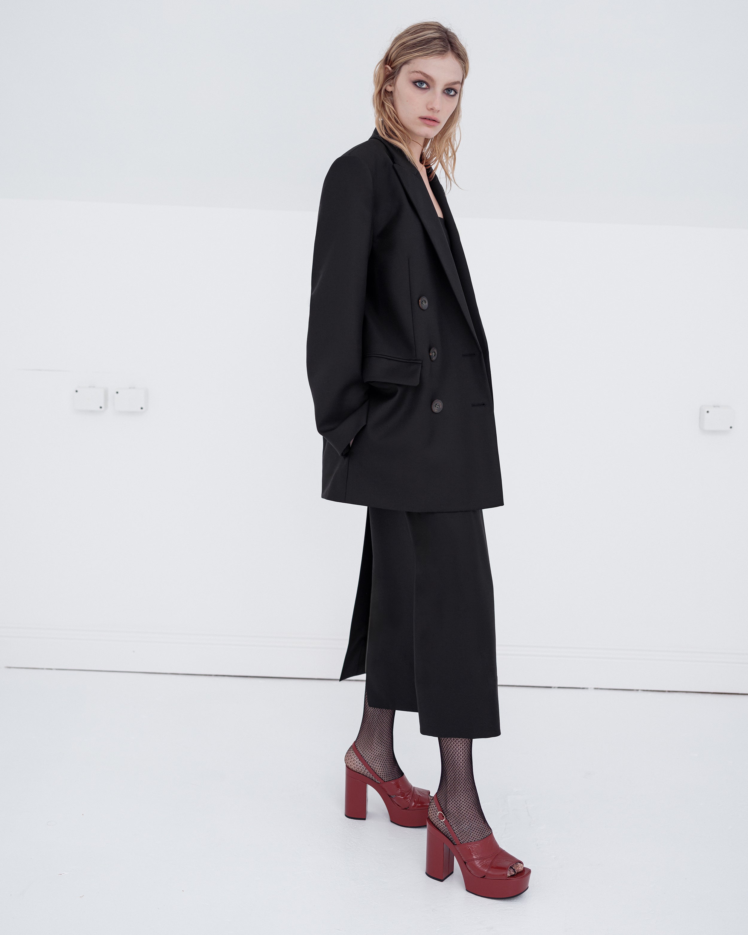Woman wearing a black Common Hours blazer and matching strapless dress on a white background