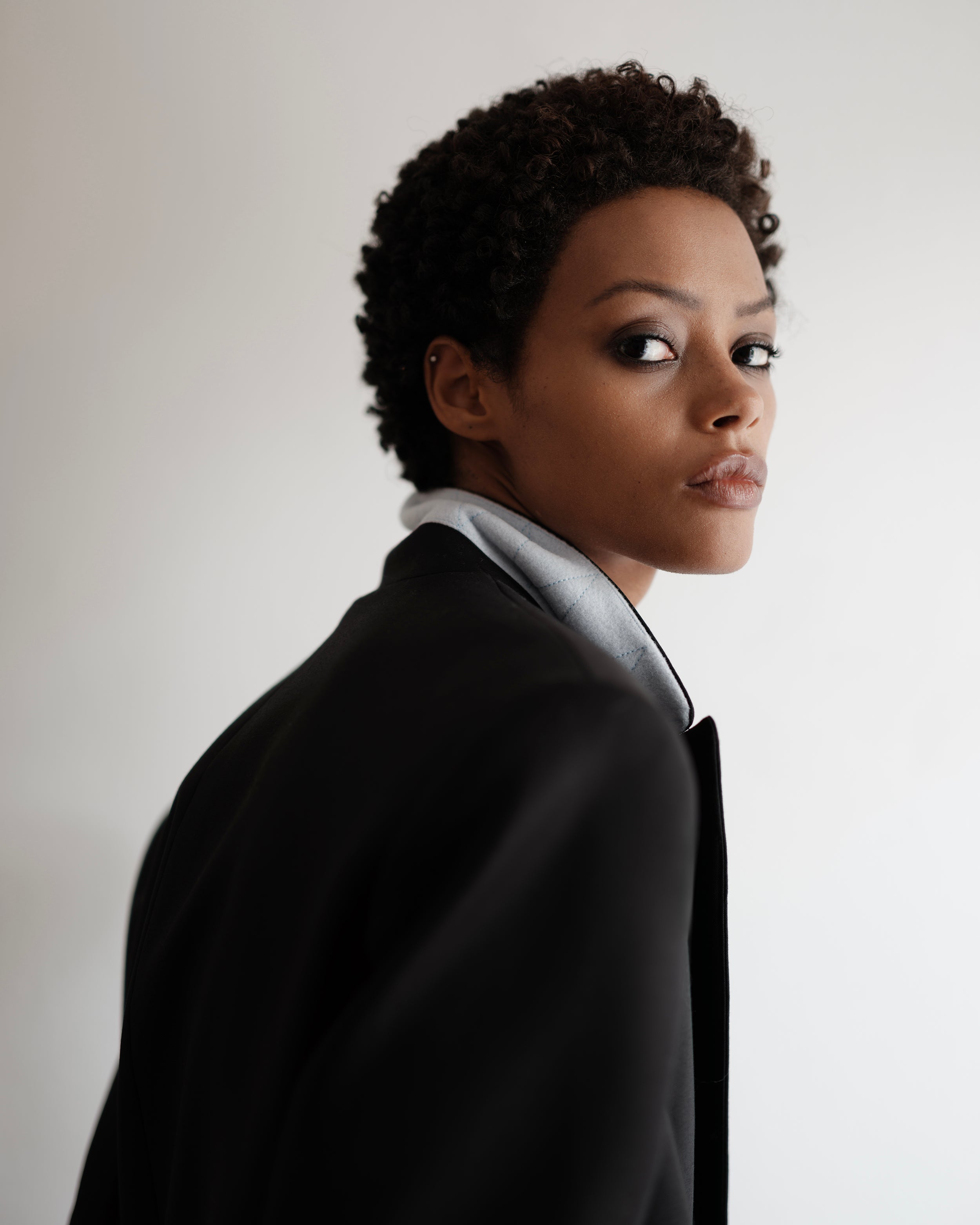 Portrait of a woman wearing a black Common Hours oversized blazer dress with contrast lapel, standing against a white background.