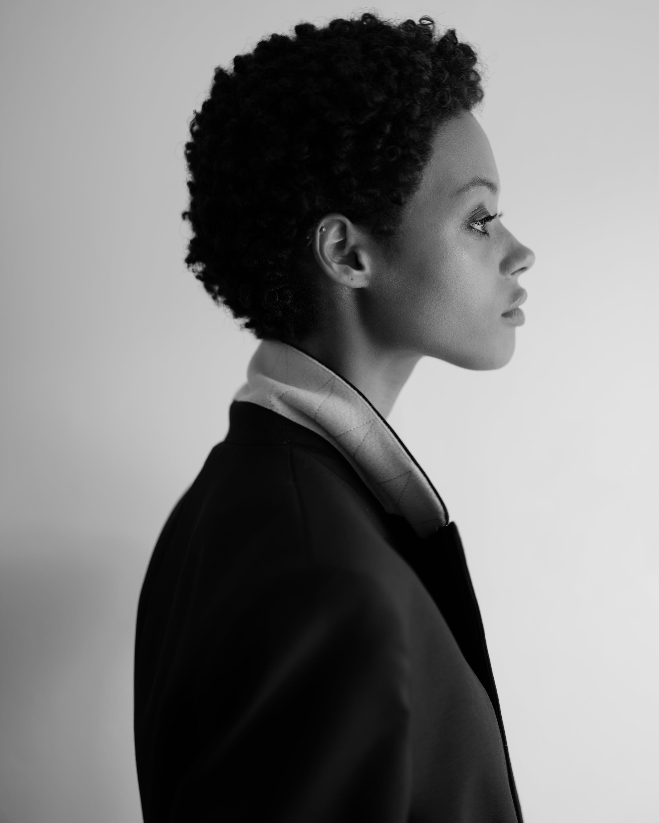 Portrait of a woman wearing a black Common Hours oversized blazer dress with contrast lapel, standing against a white background.