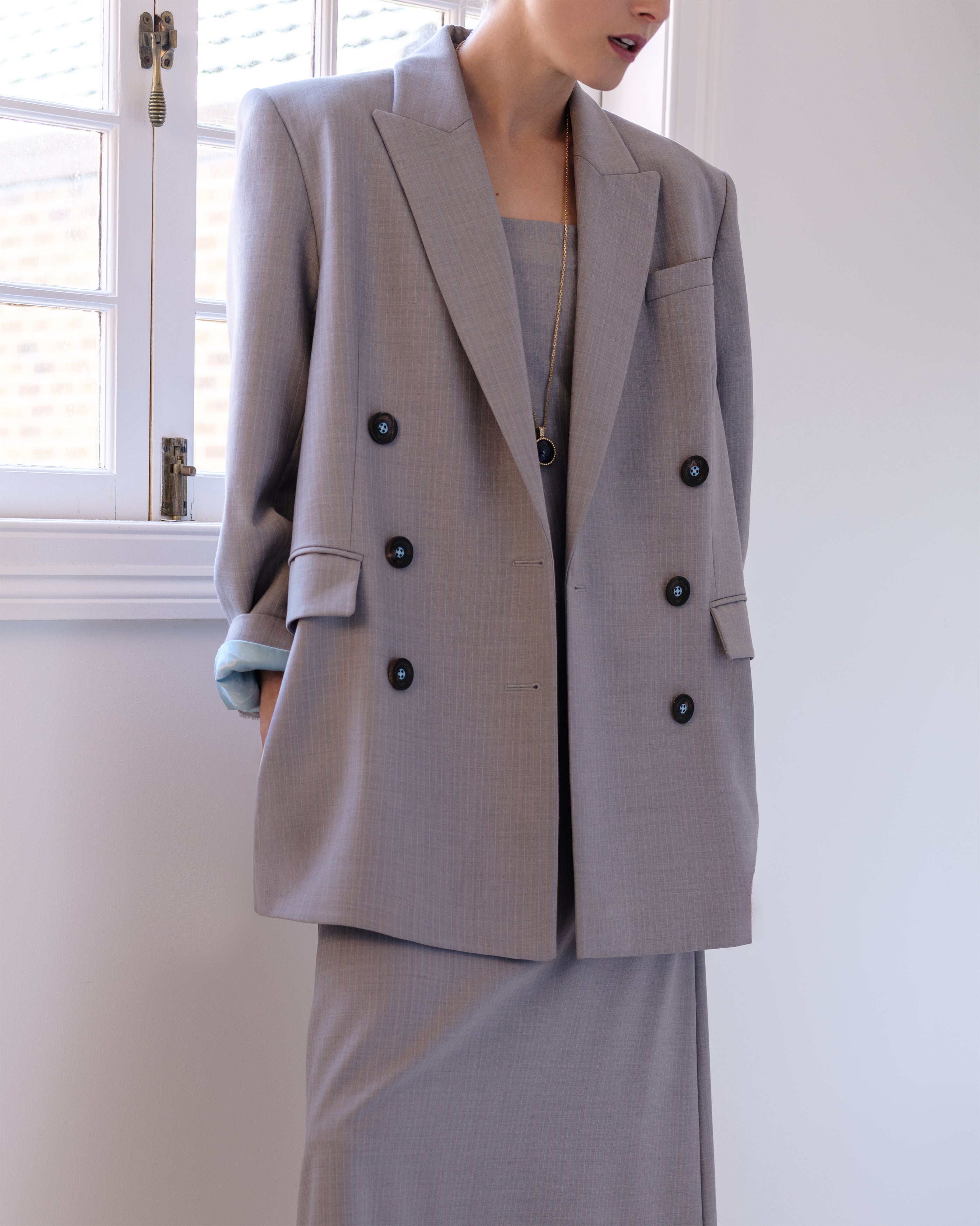 Woman wearing a gray Common Hours suit jacket and matching strapless dress.