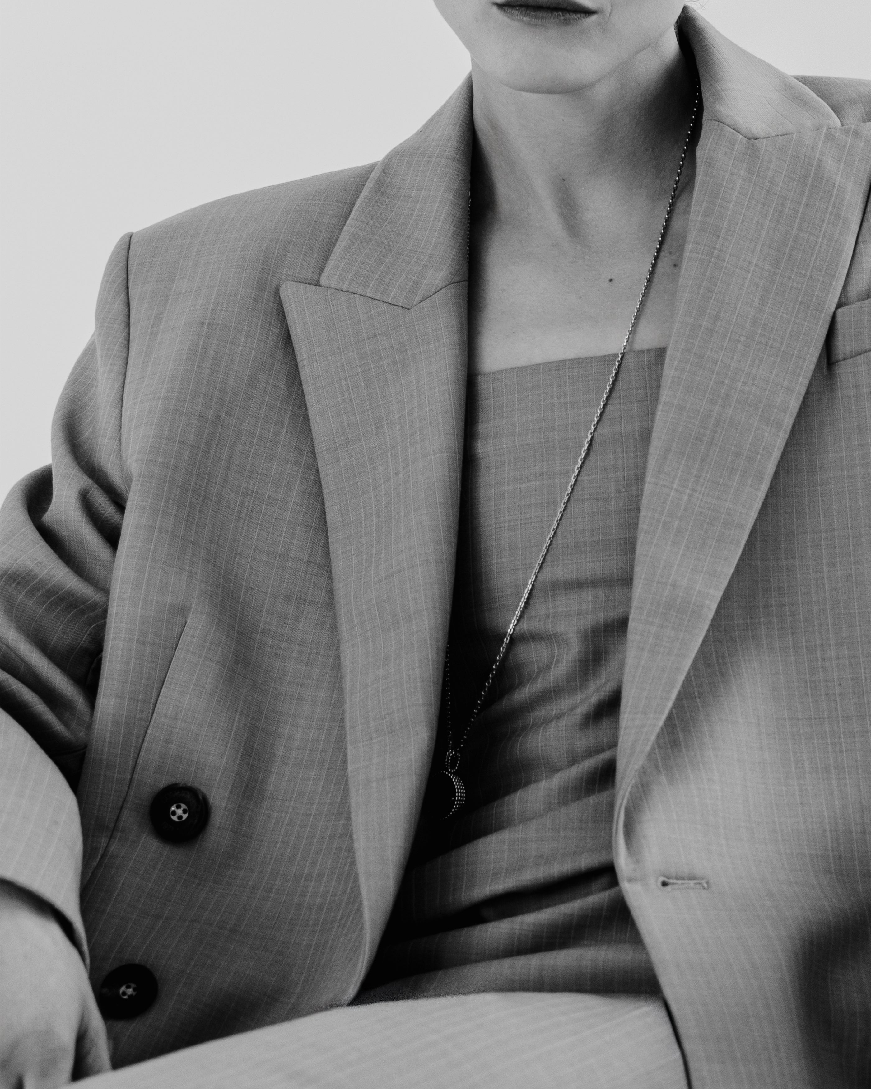 Woman wearing a gray Common Hours suit jacket and strapless dress with a plain background