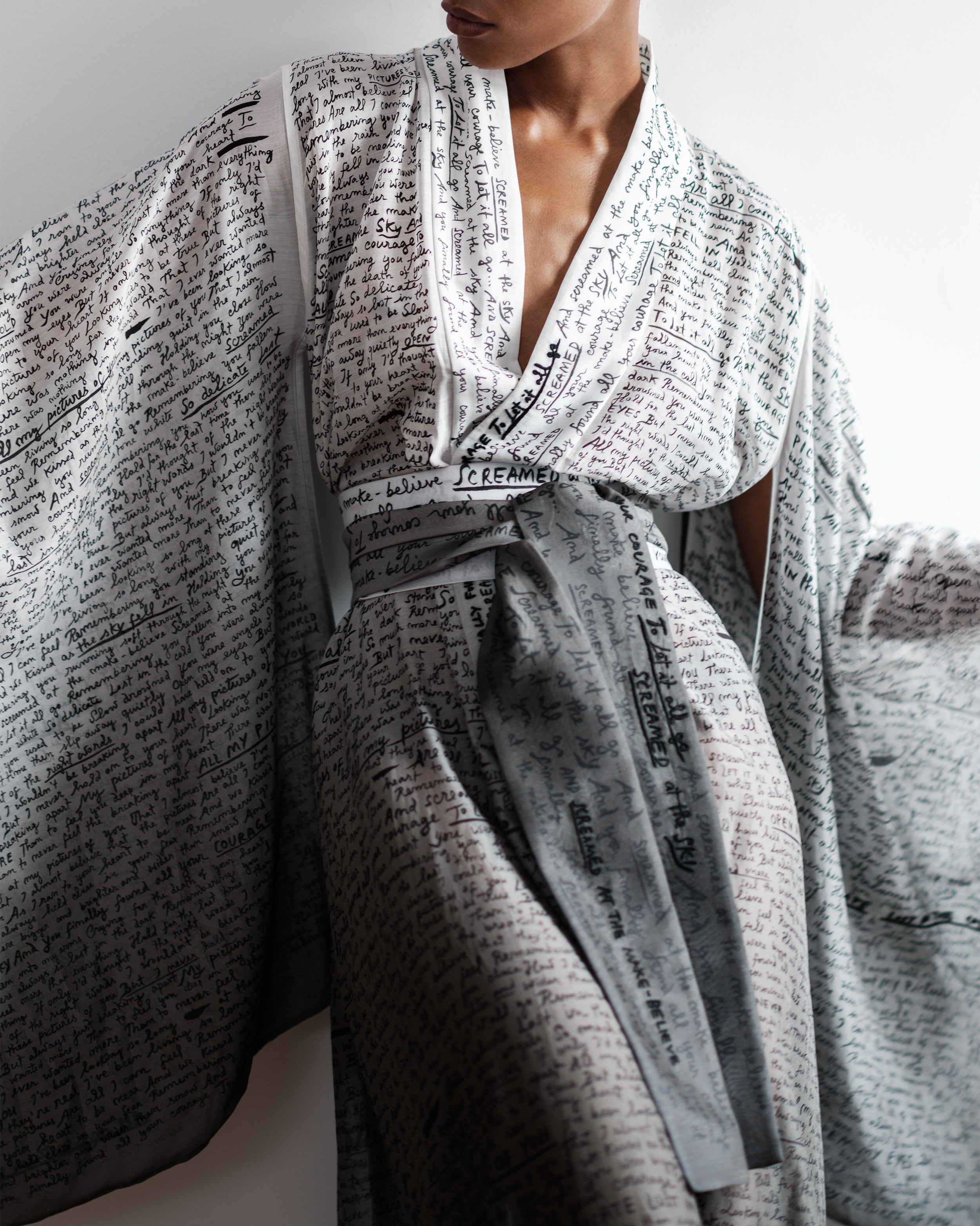 Woman wearing a Common Hours silk cotton robe with printed and hand-embroidered lyrics on a plain background