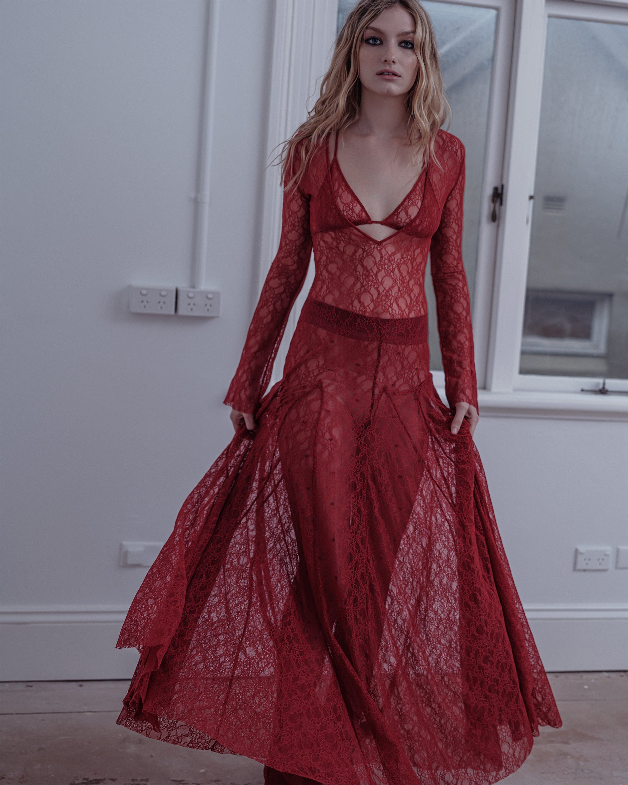Woman wearing the Cold Type Common Hours dress, red lace with long flare sleeves. 